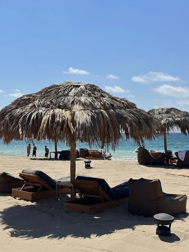 Beach scene with thatched umbrellas, lounge chairs, and people near the ocean on a sunny day