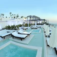 Poolside lounge chairs and umbrellas at a luxury outdoor pool area with clear blue sky and palm trees in the background.
