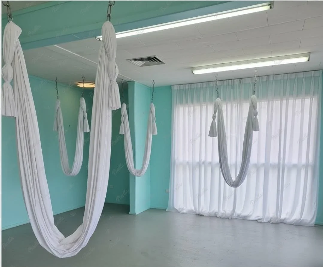An interior room with light blue walls, white curtains, and aerial yoga hammocks hanging from the ceiling.
