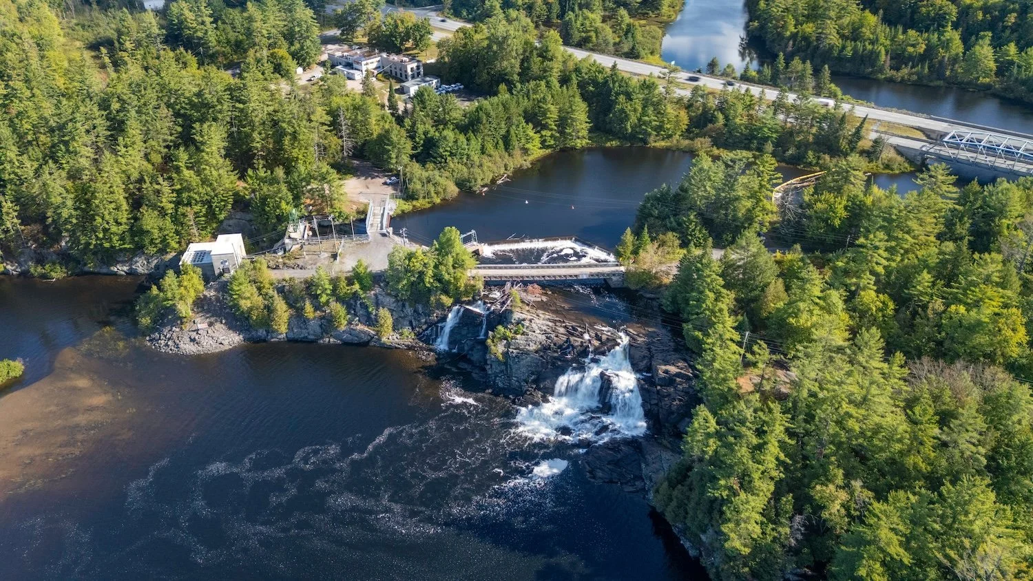 Aerial view of a Muskoka river with a waterfall, dam, and surrounding boreal forest.