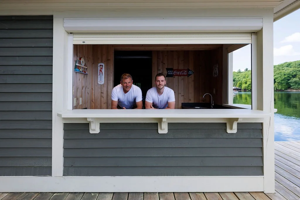 Elliott and Don Hammond of Coppergroup Renovations, leaning out from a boathouse bar on a Muskoka lake.