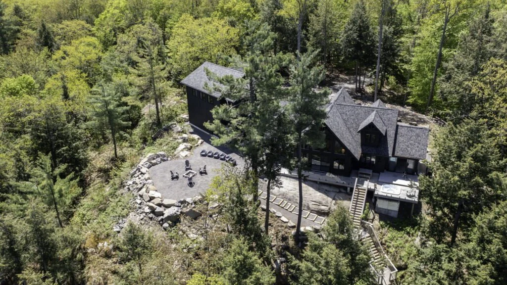 Aerial view of a luxury Muskoka cottage surrounded by forest, with a stone patio and fire pit area.