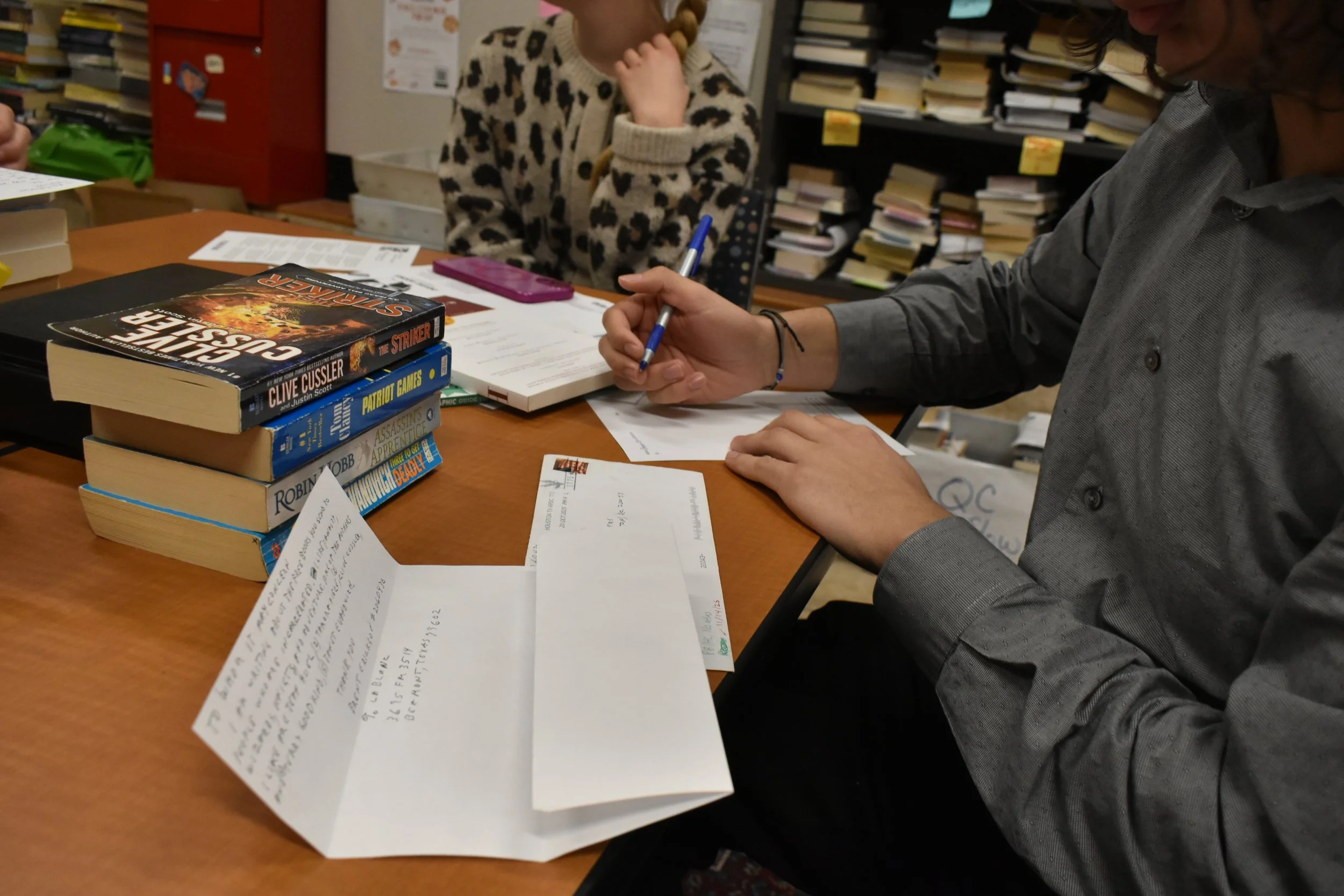 Volunteer writing a noye in response to a letter with a stack of books beside her on the table.