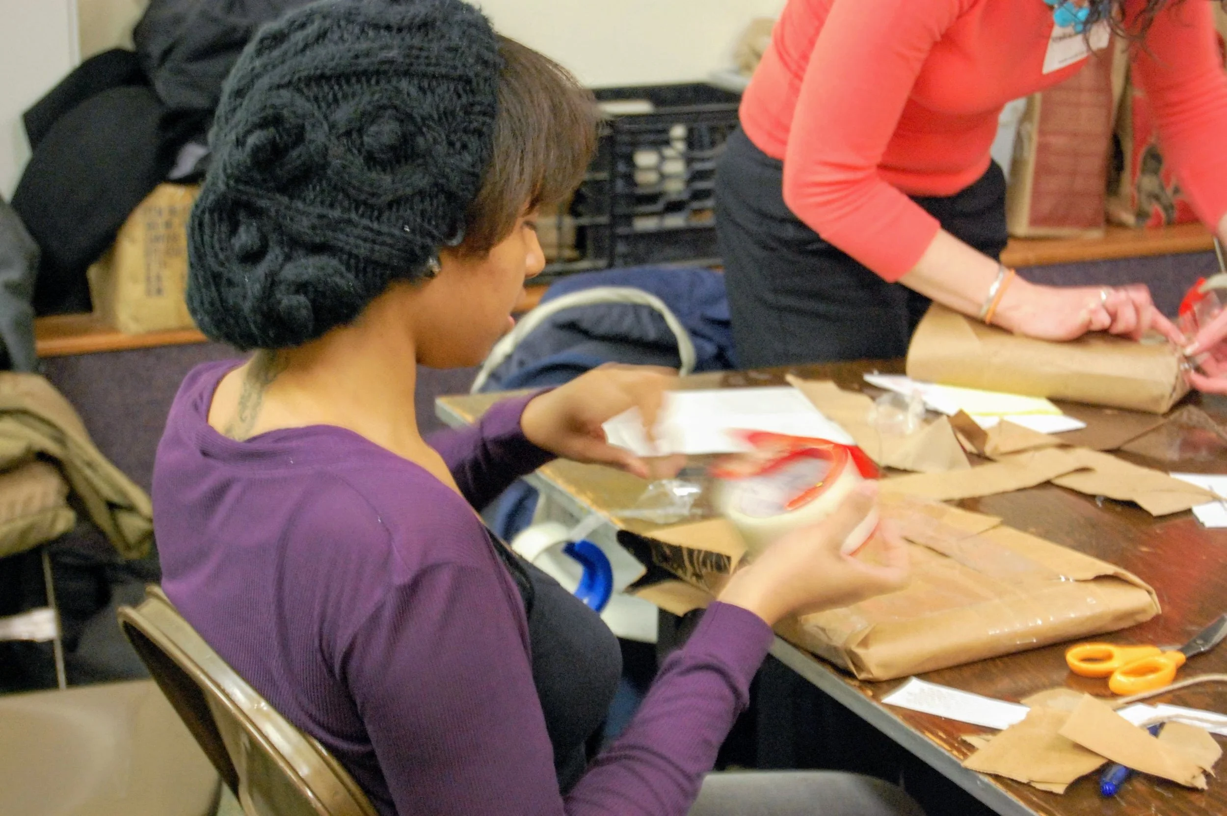 Someone siting at a table taping up packages to send.