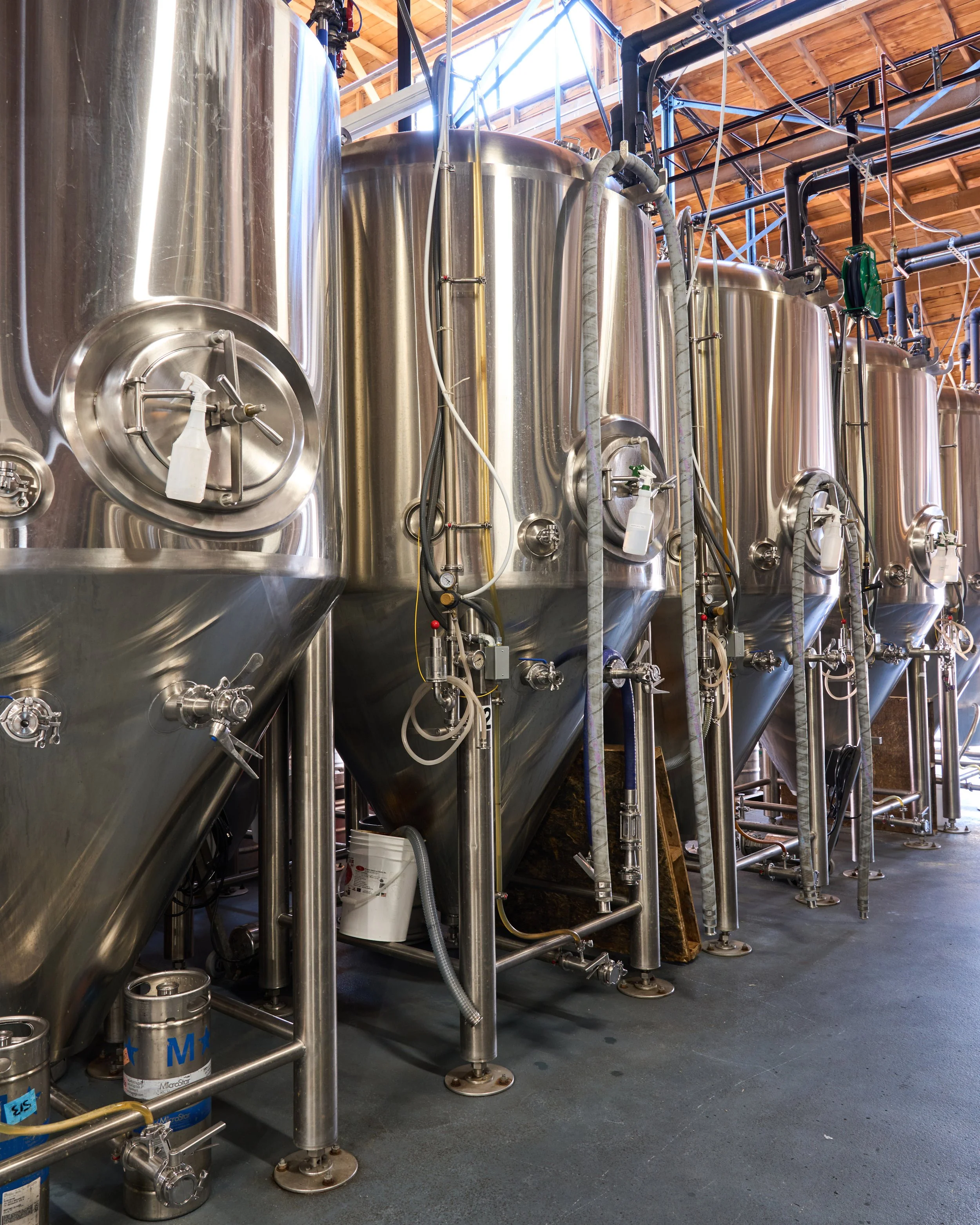 Row of large stainless steel tanks and pipes in a brewery.