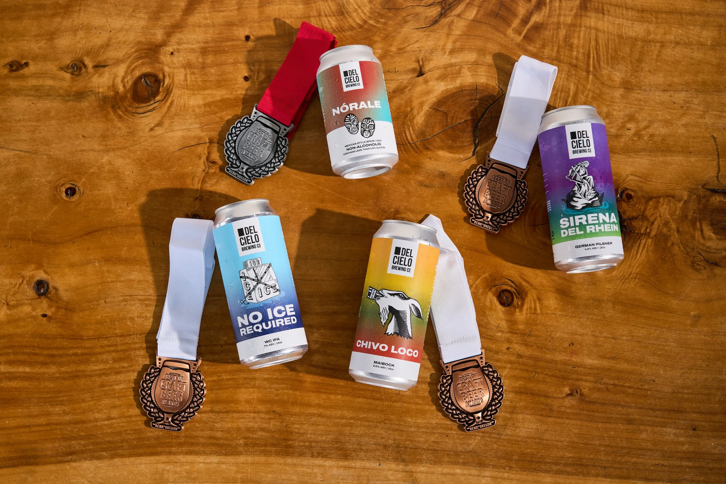 Collection of beer cans and medals on a wooden surface, with various colorful beer can labels and bronze medals with ribbons.