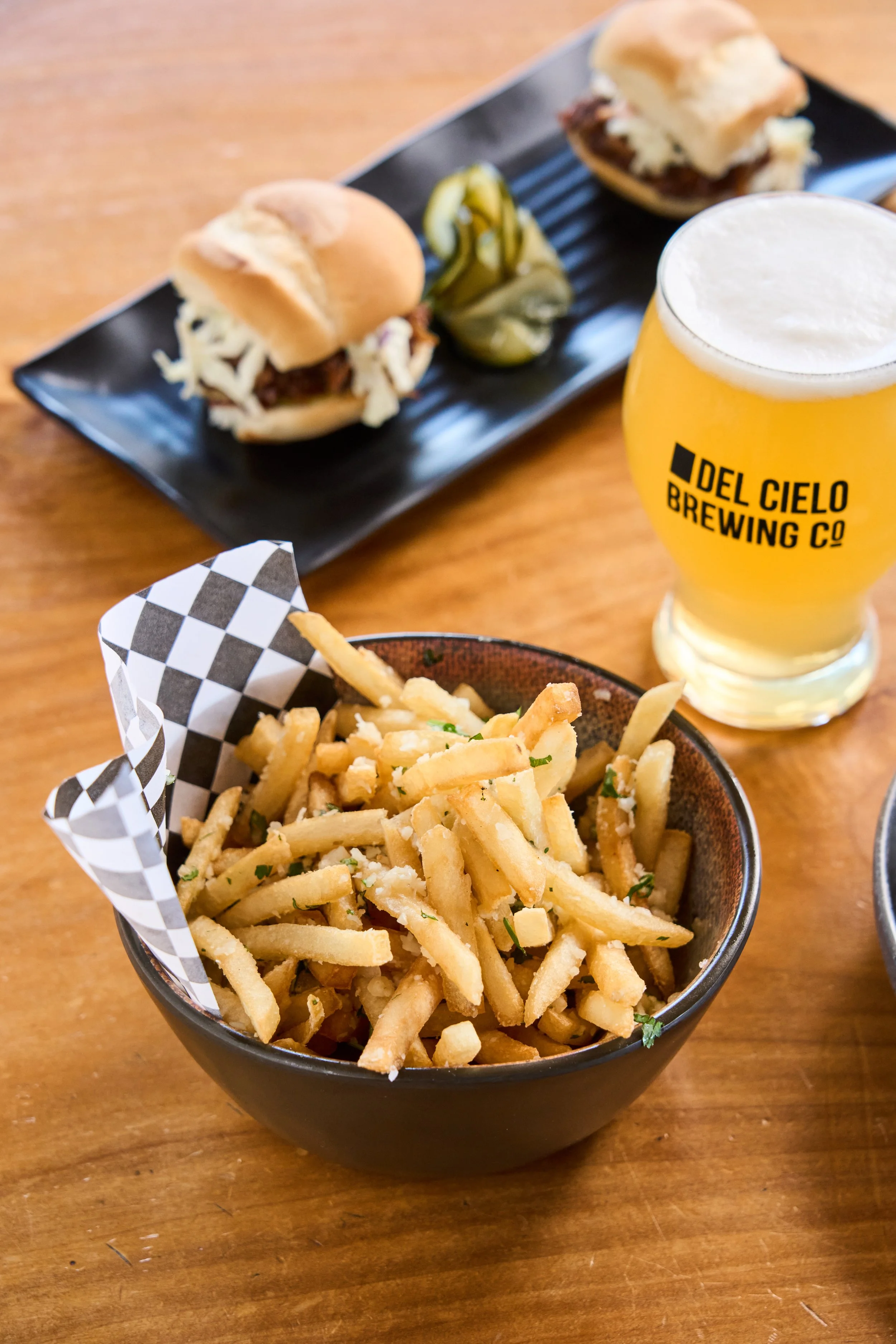 Basket of fries garnished with herbs, served with a checkered paper liner on a wooden table.