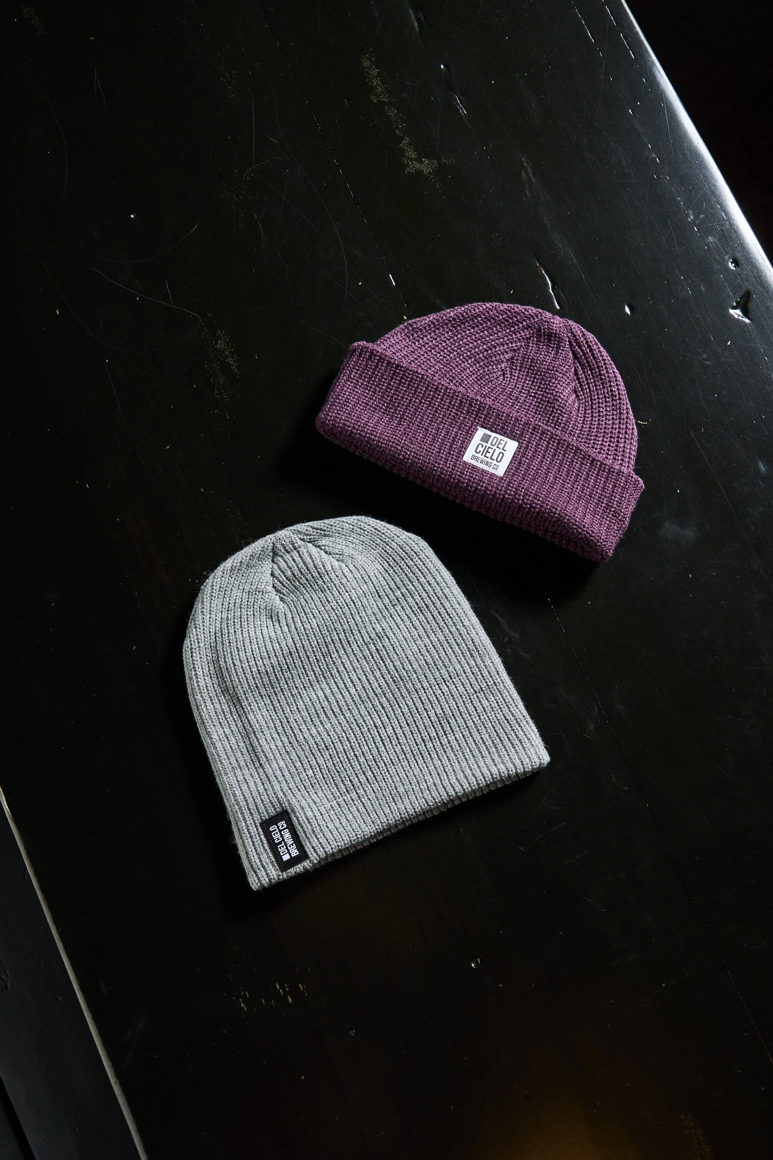 Gray knit beanie and purple knit beanie on black surface.