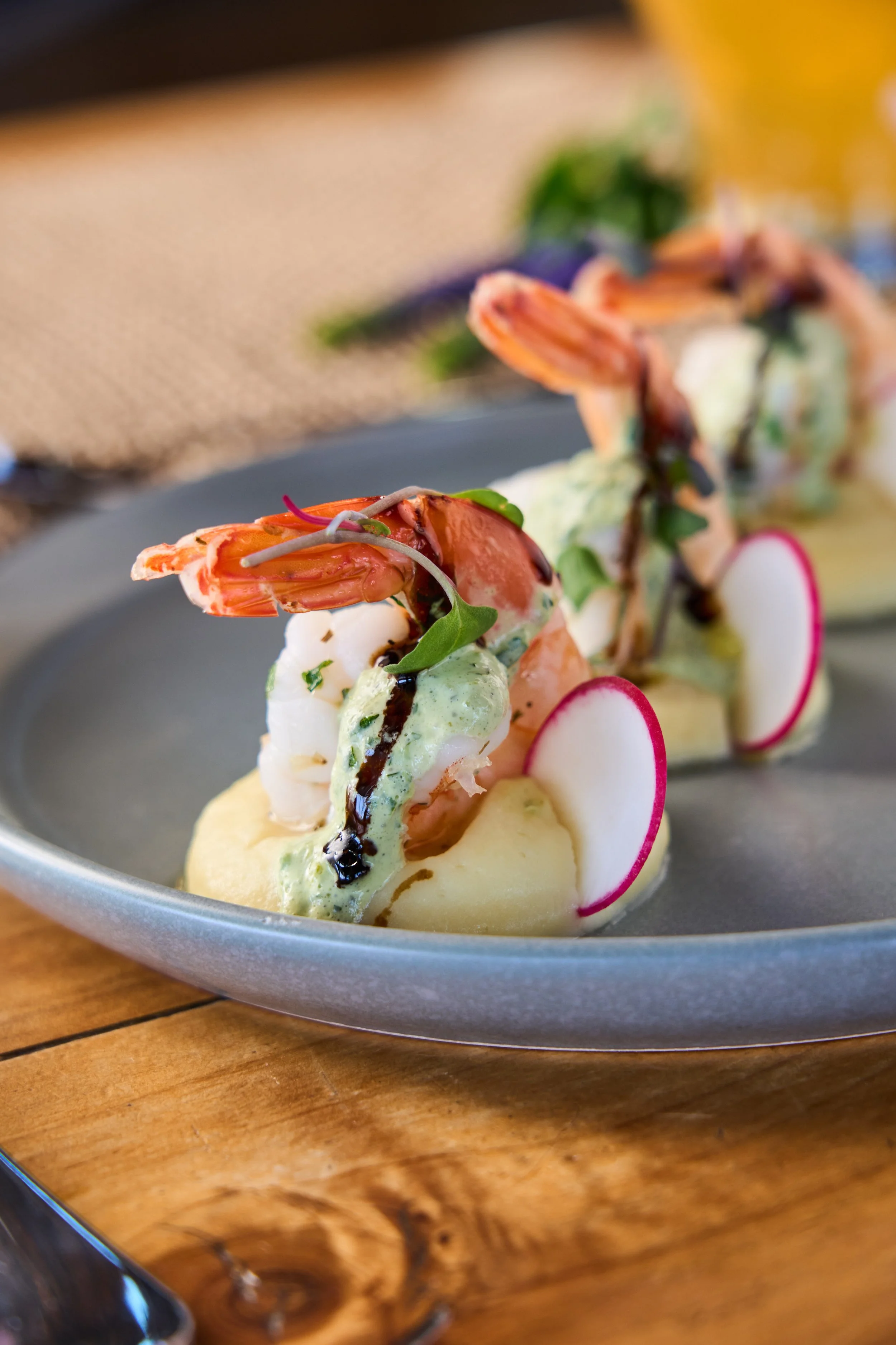 Close-up of a seafood appetizer with shrimp, radish, greens, and sauce on a round silver plate on a wooden table.