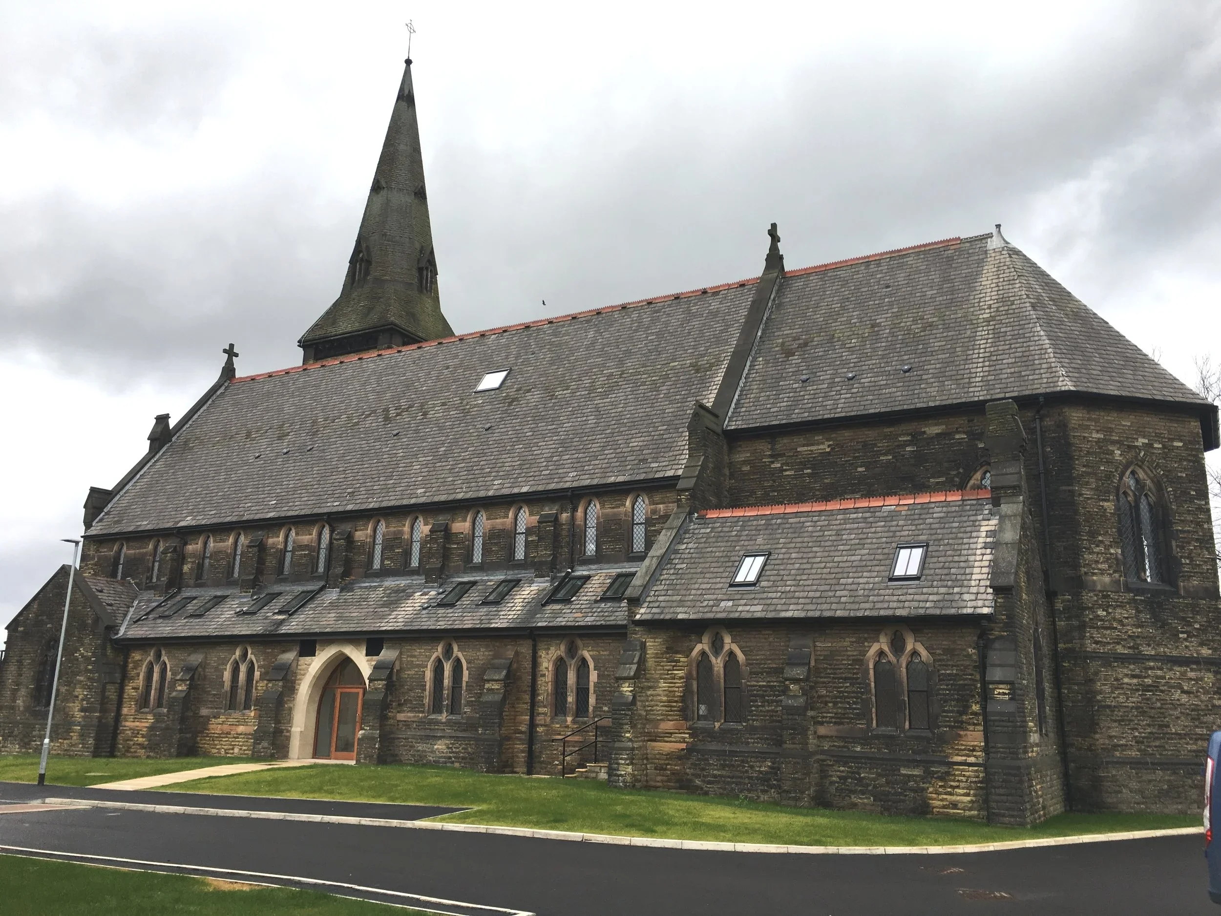 A stone church with a steep roof, arched windows, and a tall spire against a cloudy sky.