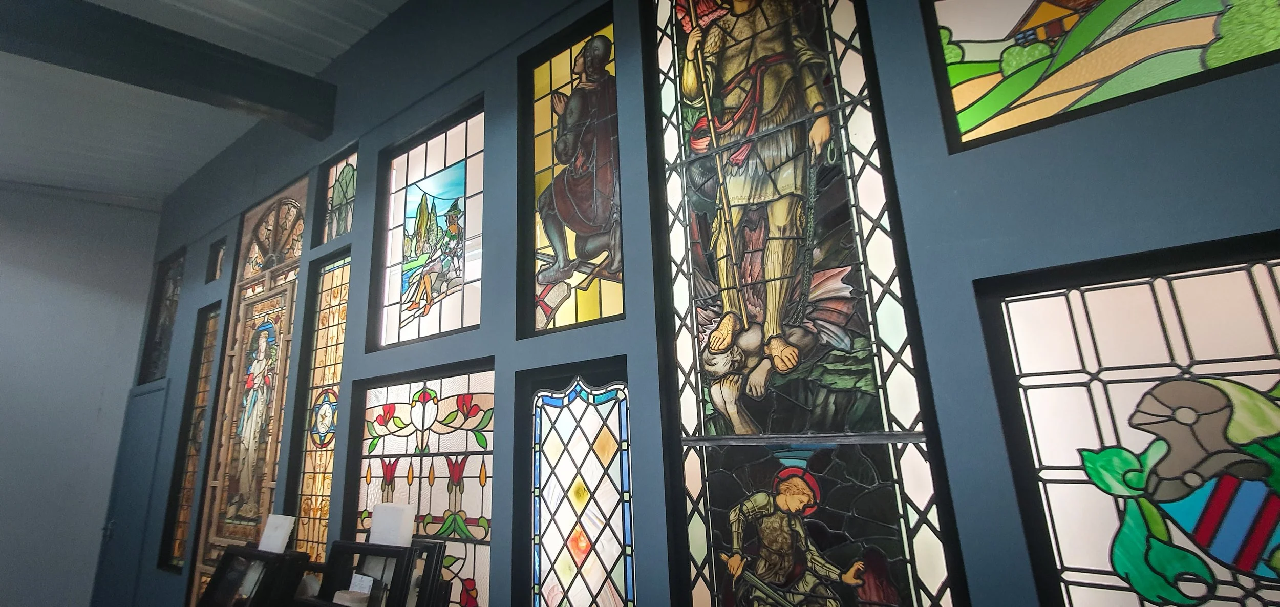 Collection of colorful stained glass windows depicting religious scenes and symbols inside a church or chapel.