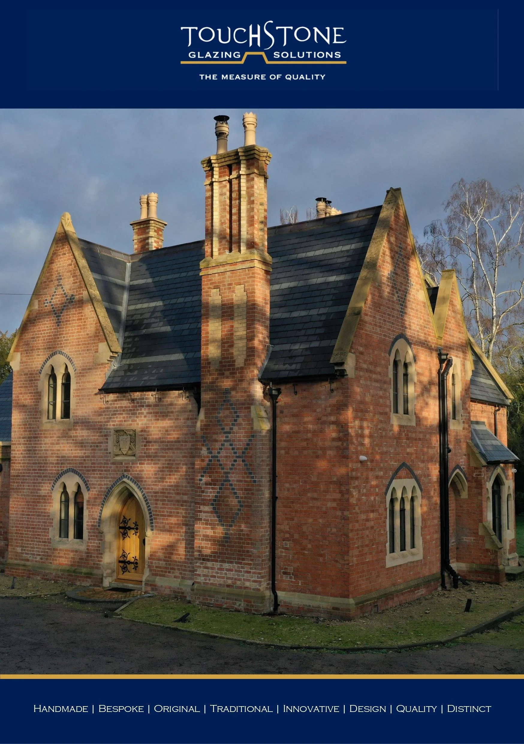 The image shows a brick building with a steep slate roof, multiple chimney stacks, arched windows, and a wooden door with decorative wrought iron. The background features a cloudy sky and trees.