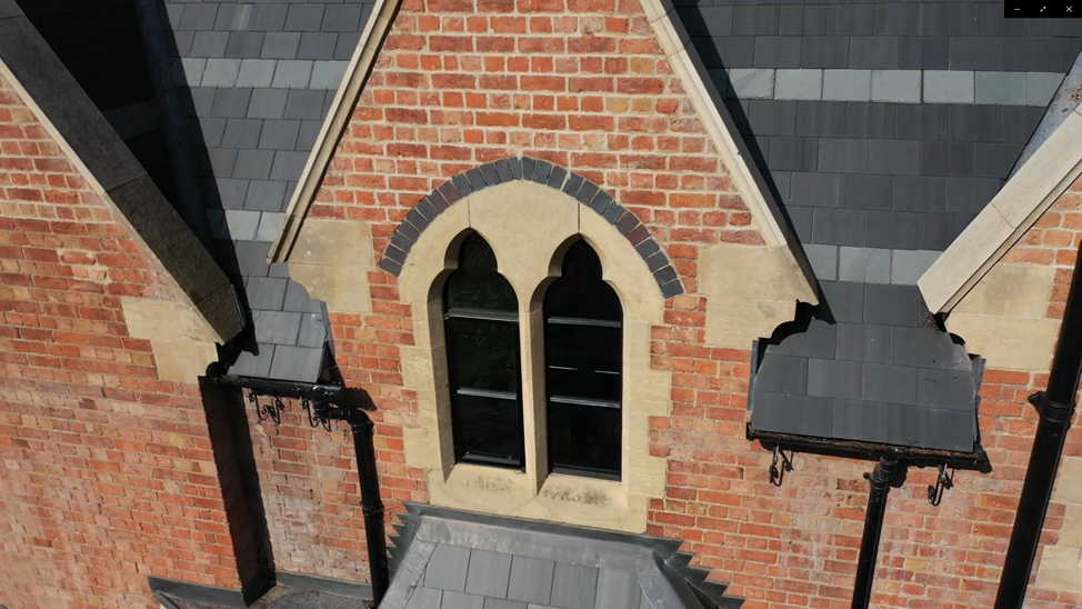 A view of a house's roof with gray shingles, a brick wall with two arched windows, and decorative brickwork around the windows.