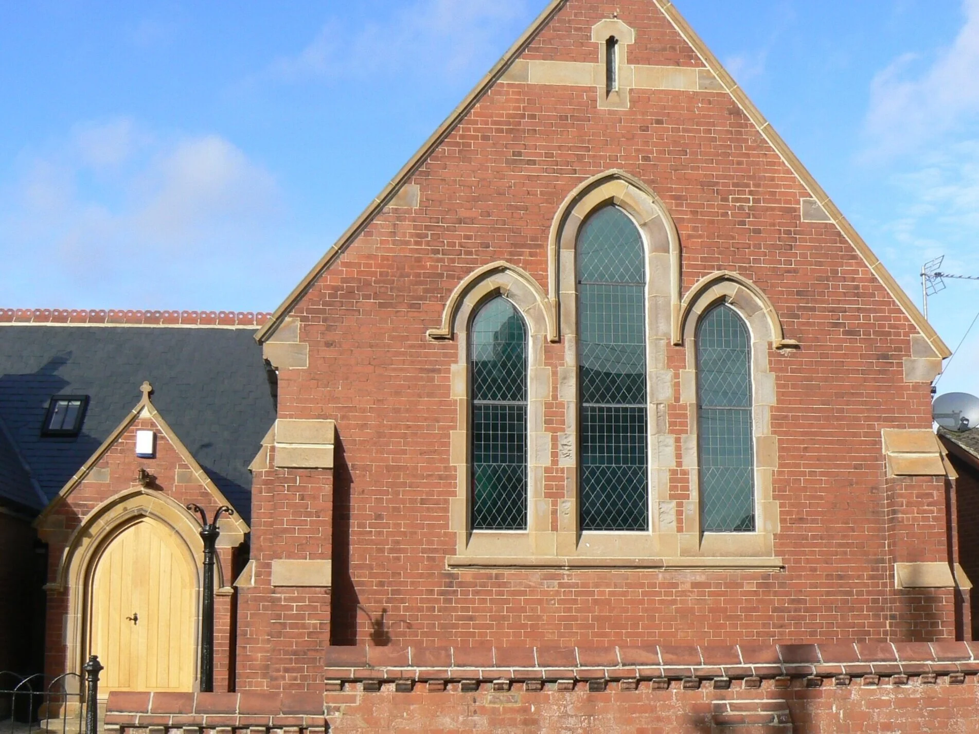 Red brick church with three tall arched windows and a wooden doorway, set under a blue sky.
