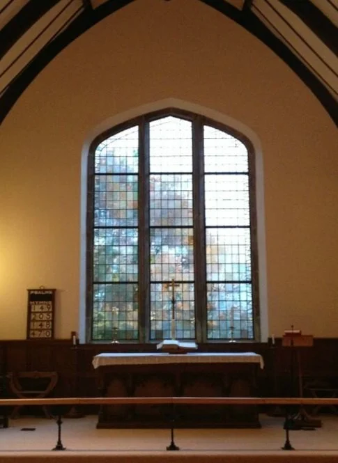 Religious altar area inside a church with a large stained glass window, cross, open book, and worship items.