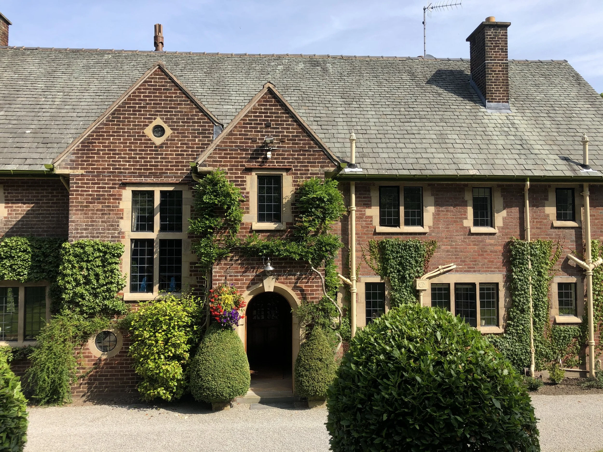 Brick house with multiple windows and ivy plants, surrounded by well-maintained bushes and a gravel pathway.