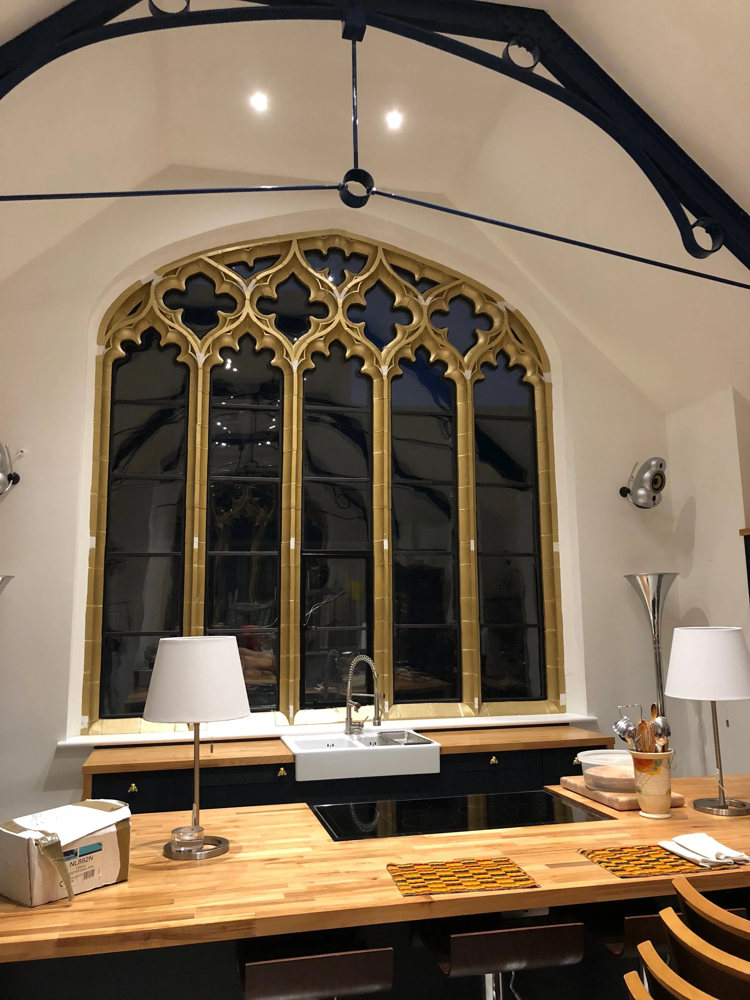 A kitchen with a large Gothic-style window, a white farmhouse sink, a wooden countertop, two white lamps, and modern appliances.