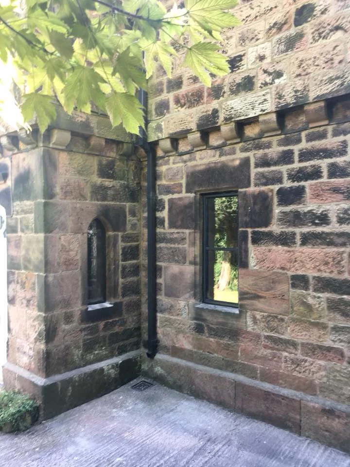 Close-up of a stone building wall with two windows and a black gutter pipe.