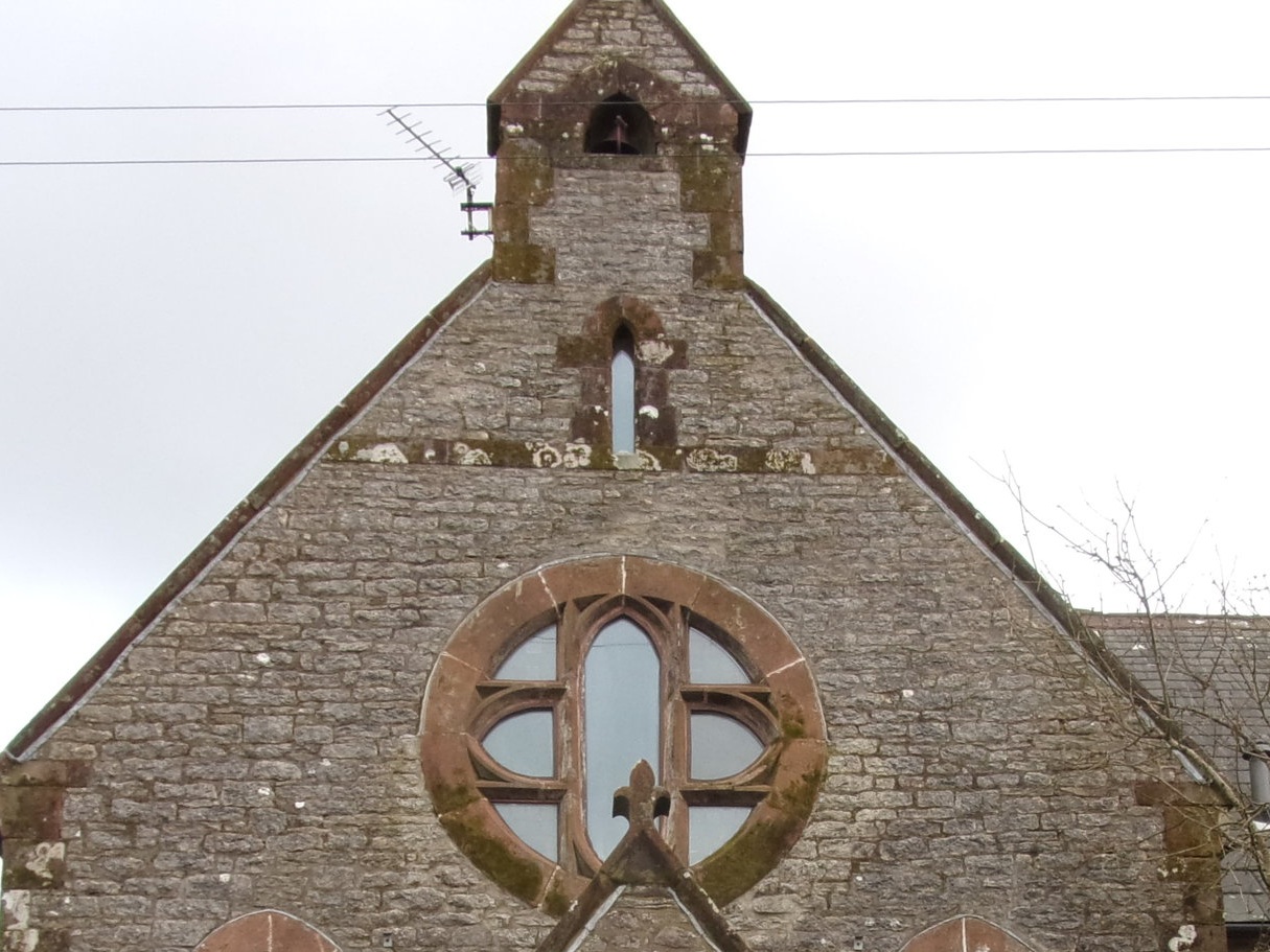 The front of a stone church with gothic-style windows and a small bell tower on top.
