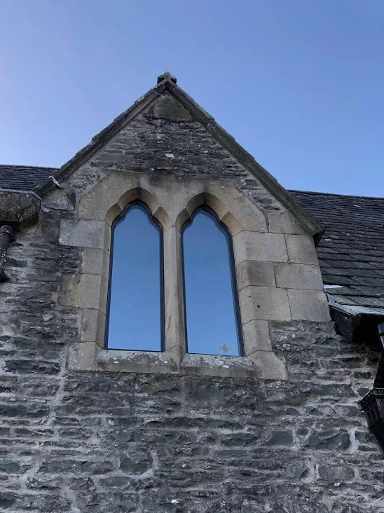 Close-up of an old stone church wall with two arched windows and a clear blue sky above.