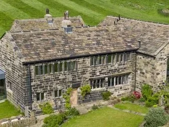 A large stone historic building with a grassy lawn and garden in front, situated in a lush green setting.