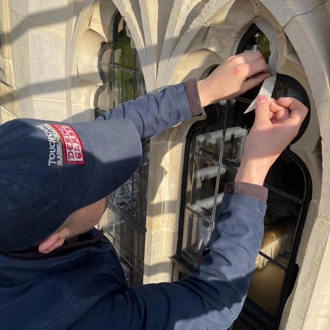 A person is cleaning a stained glass window on a building with a cloth, using their hands to wipe the glass.