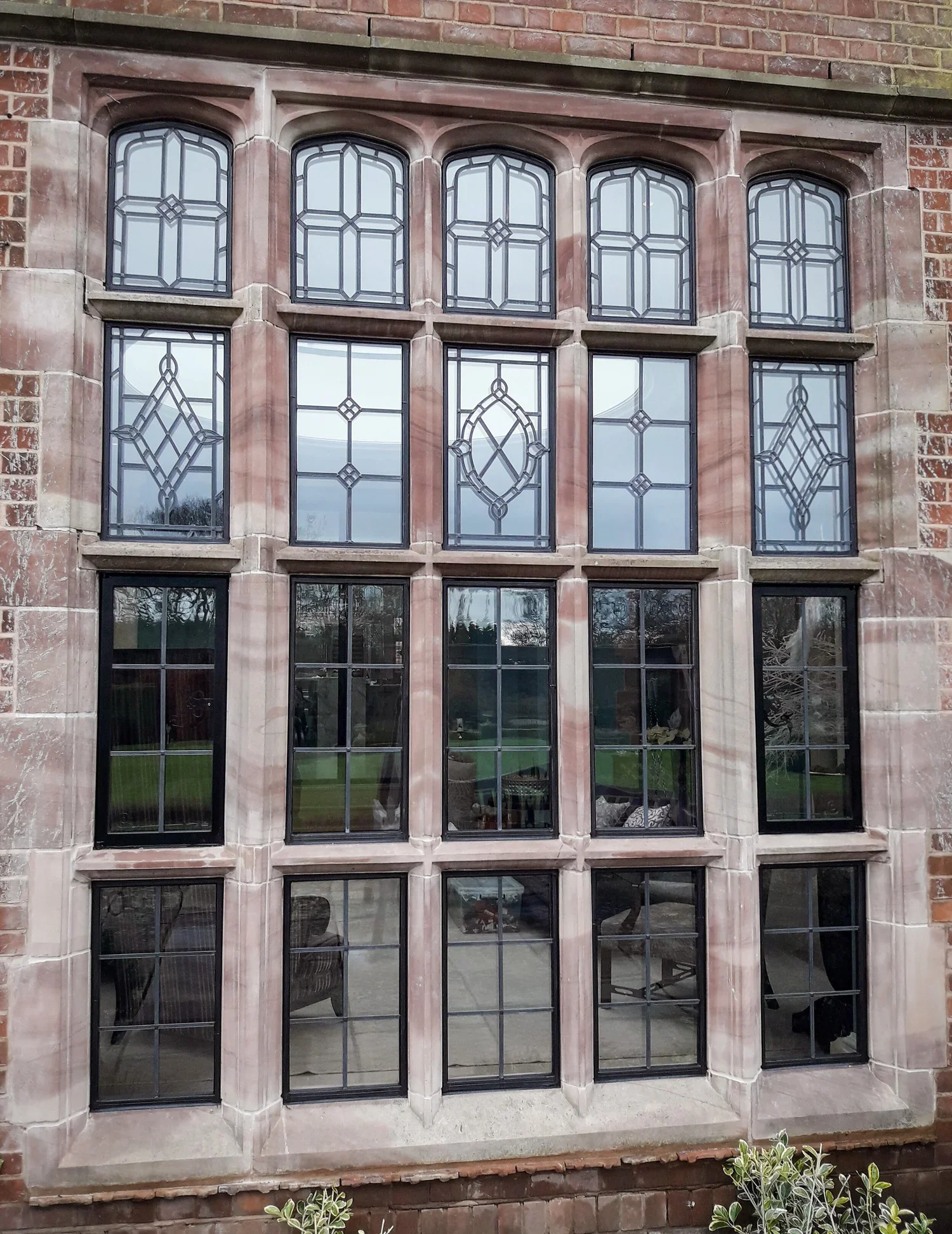View of a building with a large stained glass window grid, featuring geometric patterns, set in brick and stone architecture.