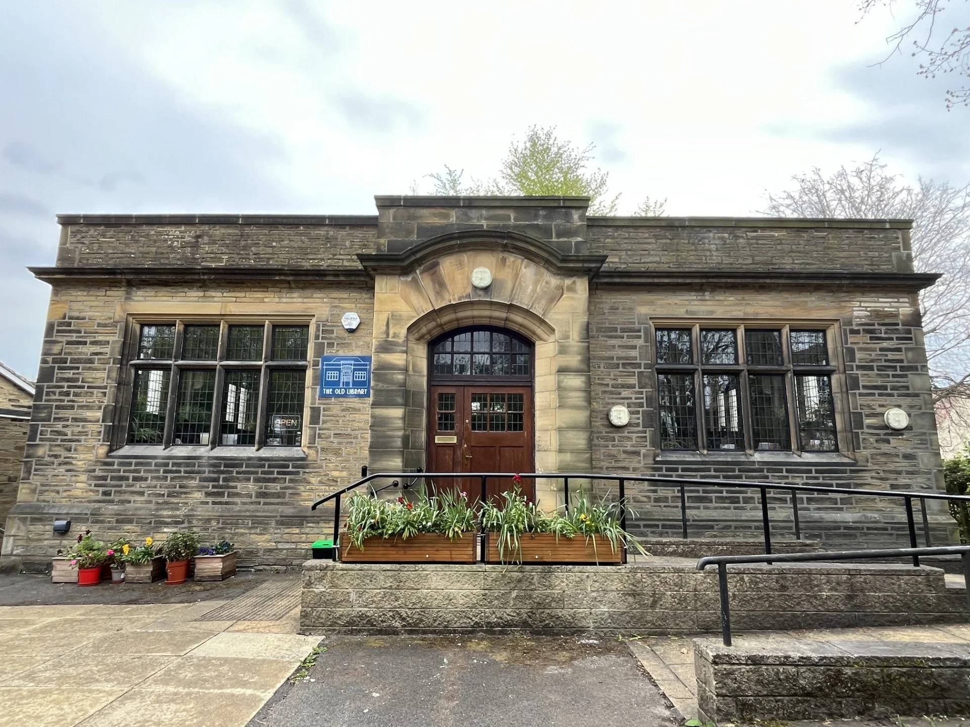 Front facade of a historic stone building labeled 'The Old Library' with flower pots and planters in front.