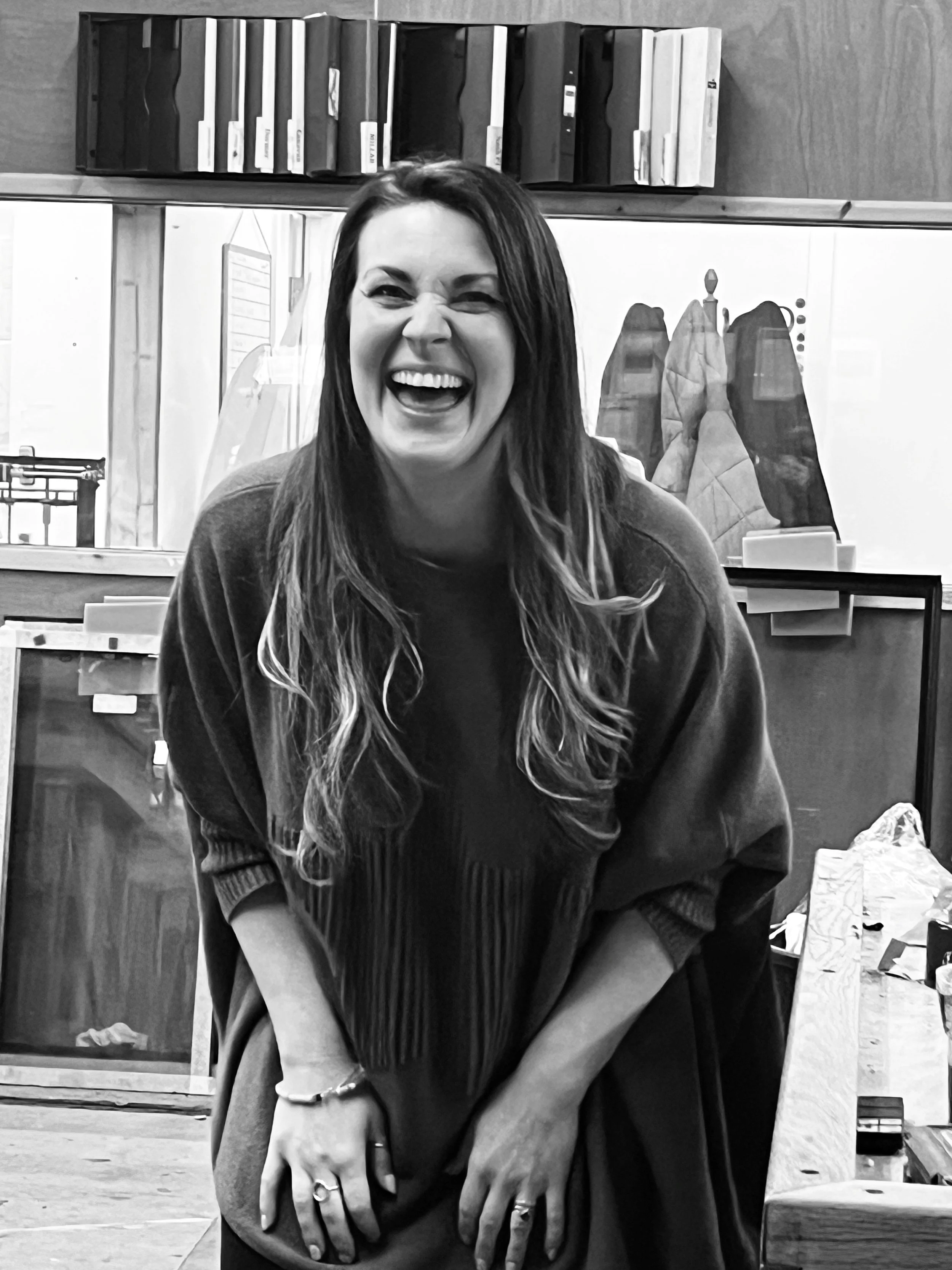 Woman with long hair laughing and leaning forward in front of a workbench in a workshop
