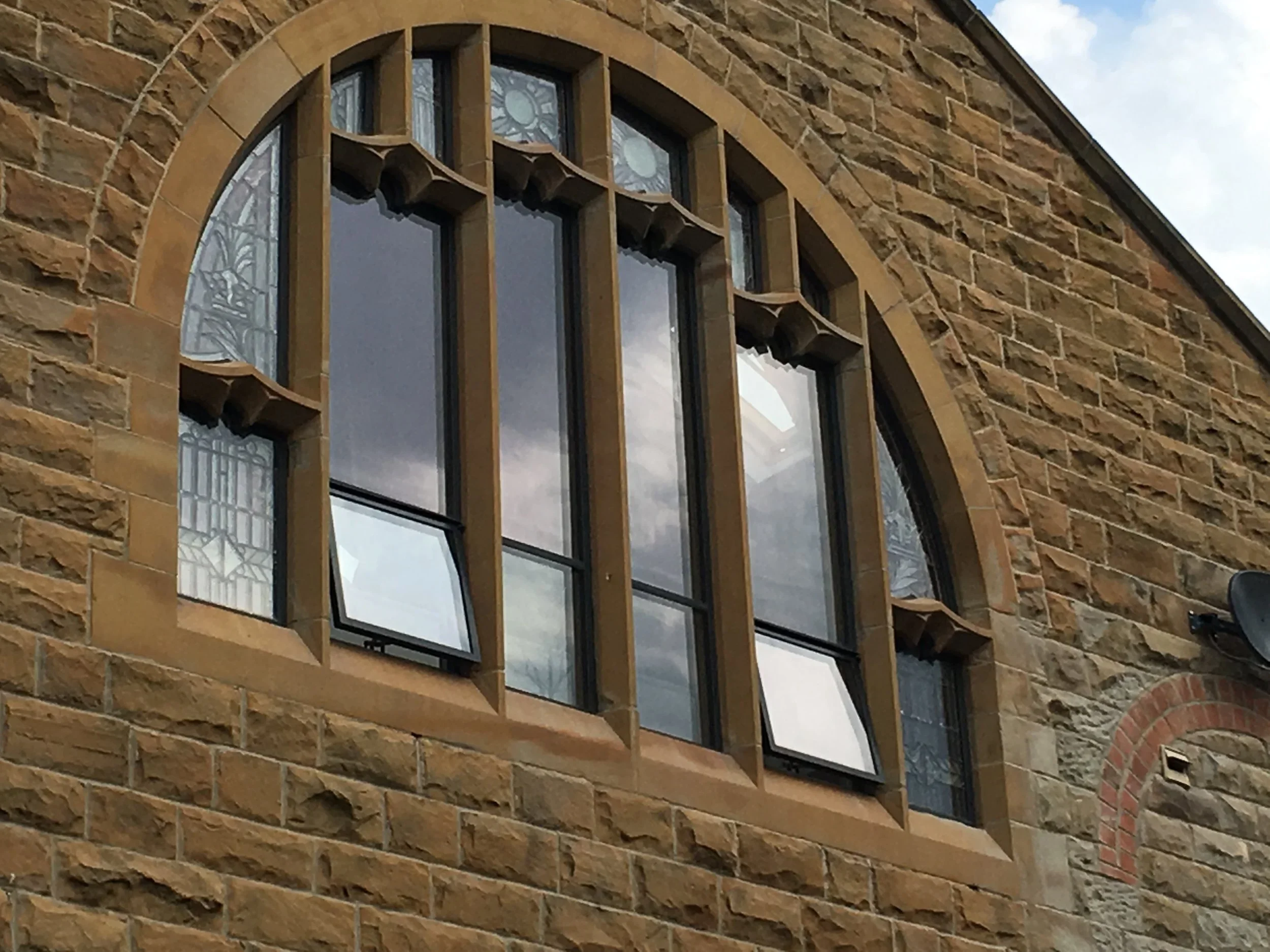 Close-up of a building's brick wall with a decorative arched window featuring stained glass and multiple panes.