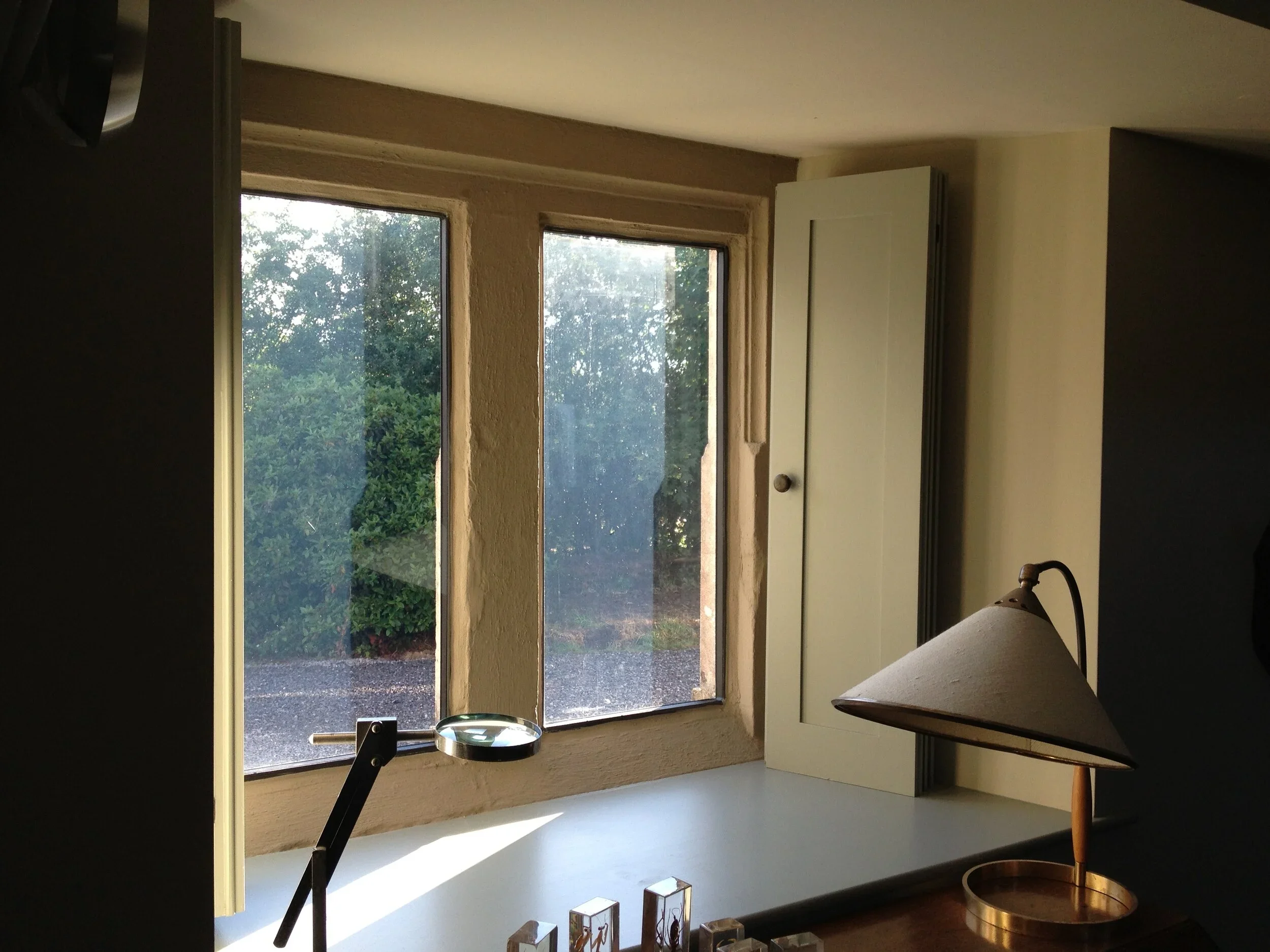 A window with a view of trees outside, a desk lamp, a candle holder, and four small animal figurines on the desk inside.