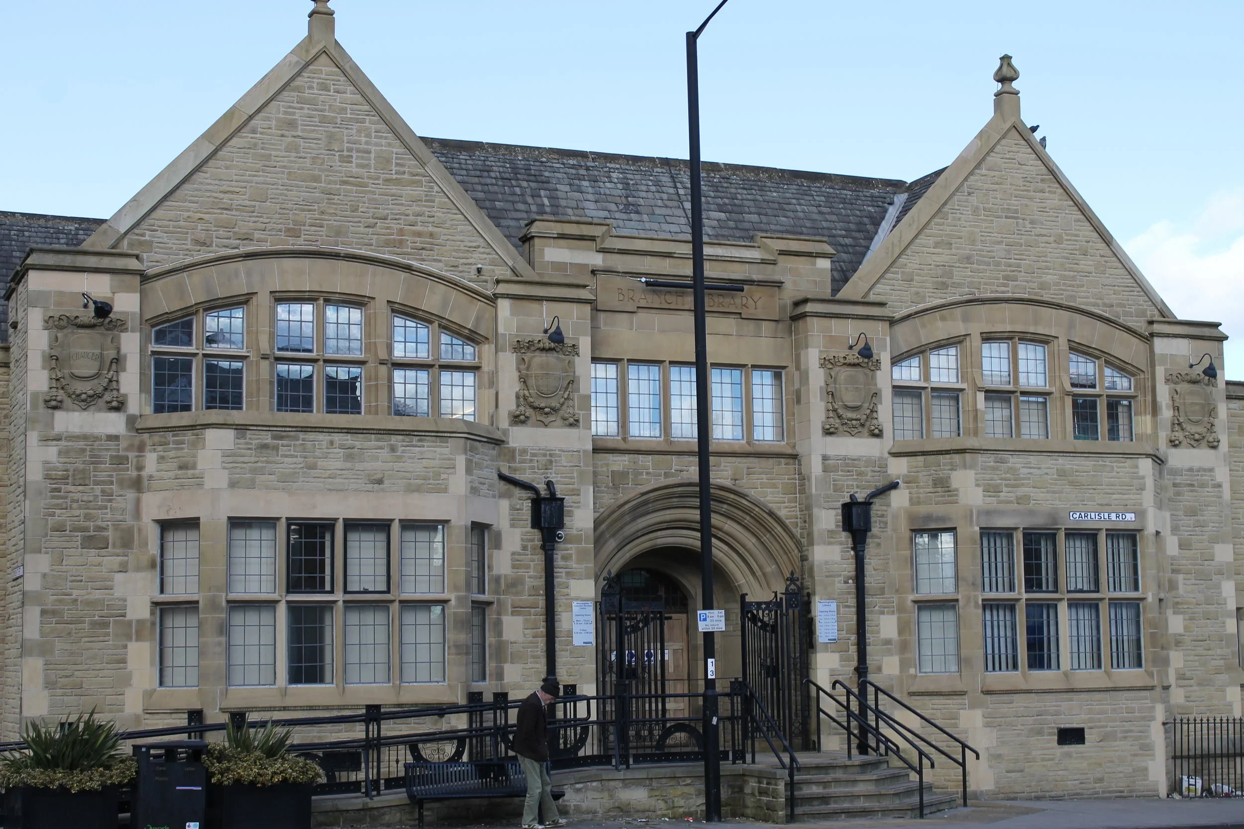 A historic stone building labeled 'Branch Library' with arched windows, decorative stone carvings, and a gated entrance, located on Carlisle Road.