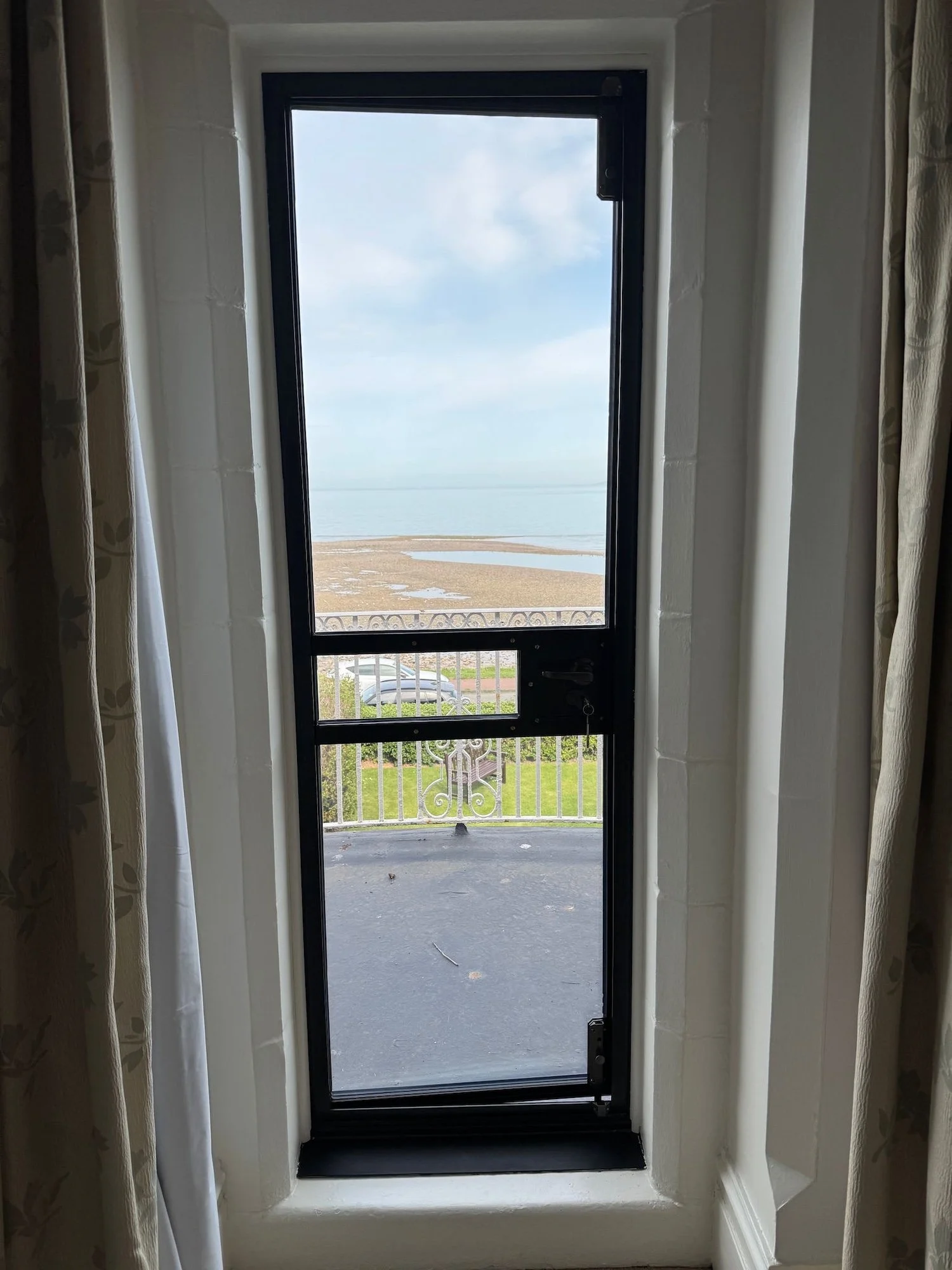 View through a glass door leading to a balcony with a view of a beach and water.