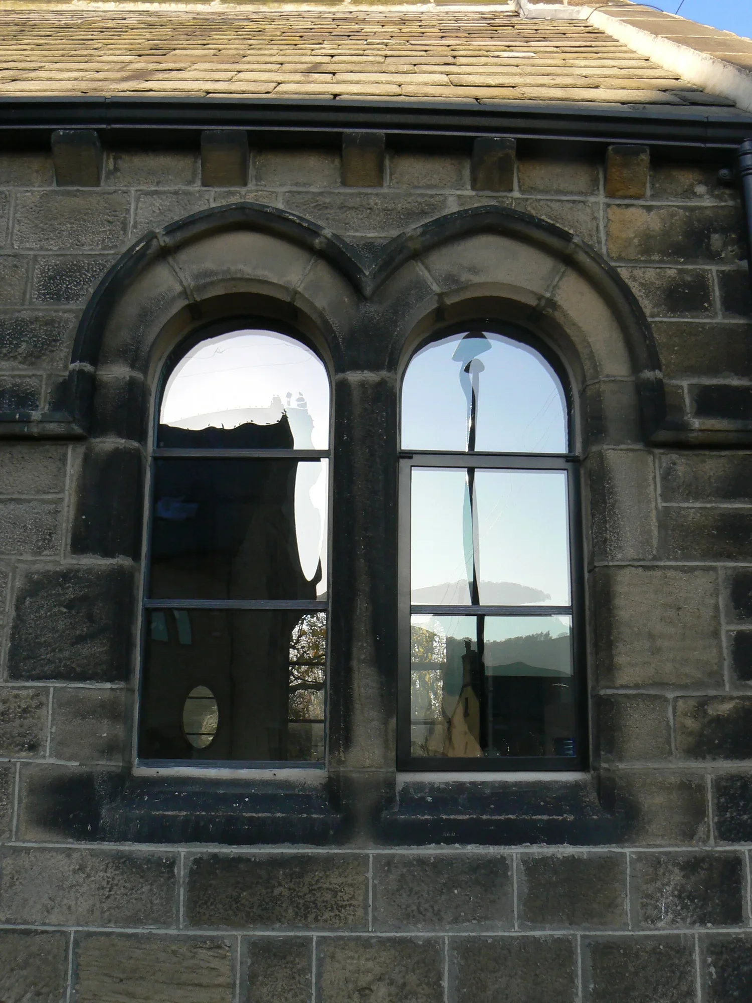 A close-up view of a stone building with an arched window and the reflection of a mountain landscape in the glass.