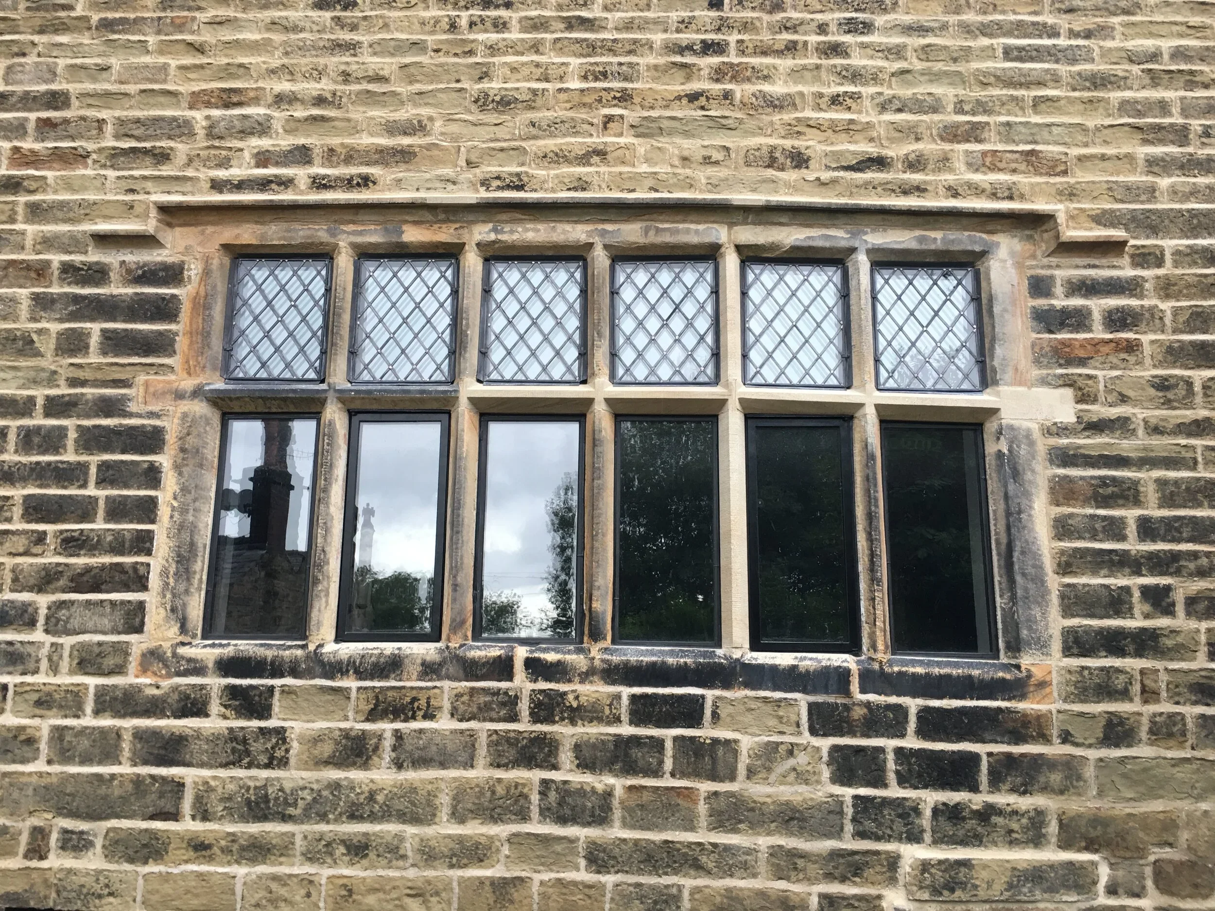 A brick wall with a set of six rectangular windows with black metal crossbars to prevent breakage.