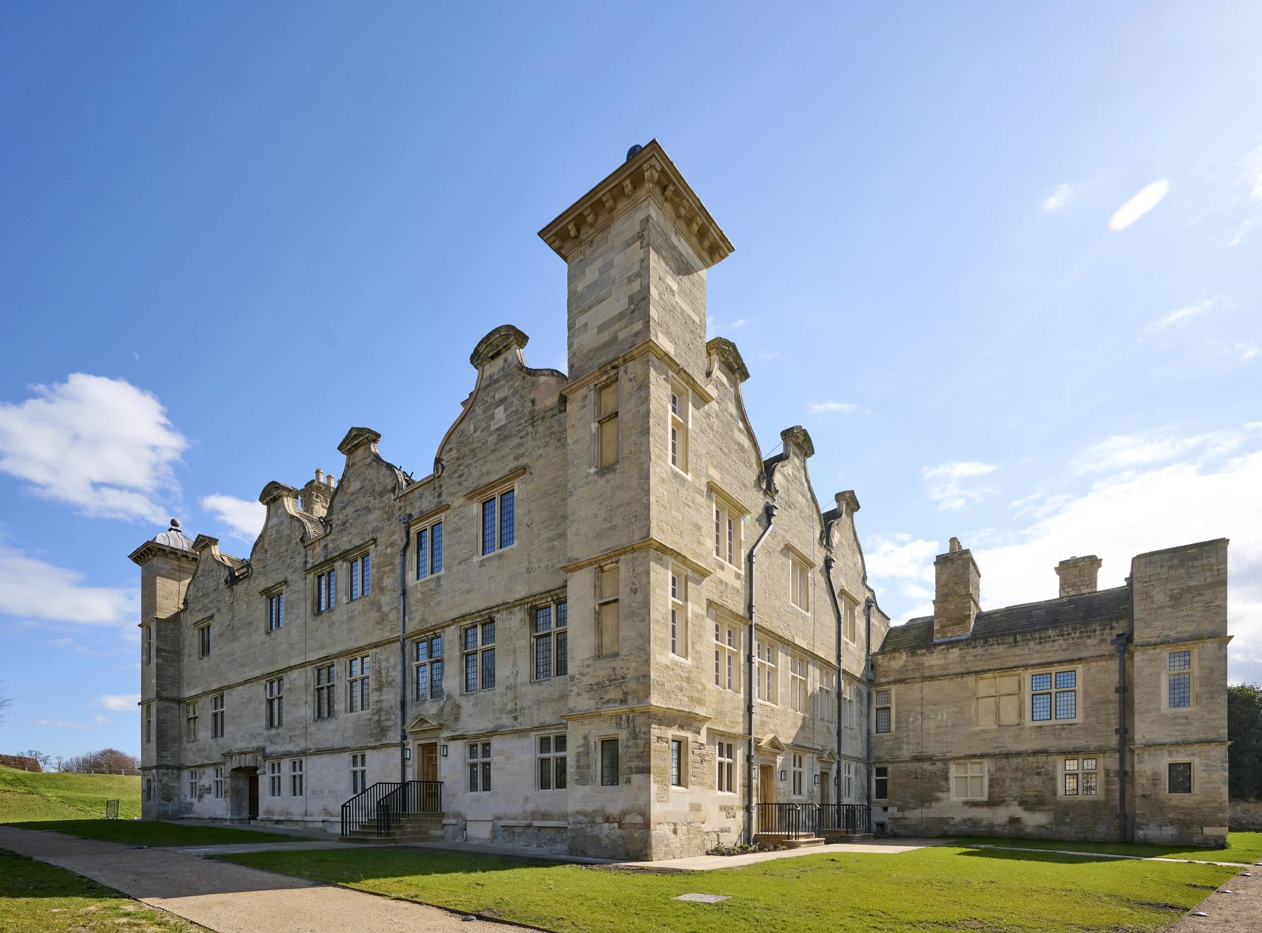A historic castle with beige stone walls and tall windows, set against a bright blue sky with some clouds.