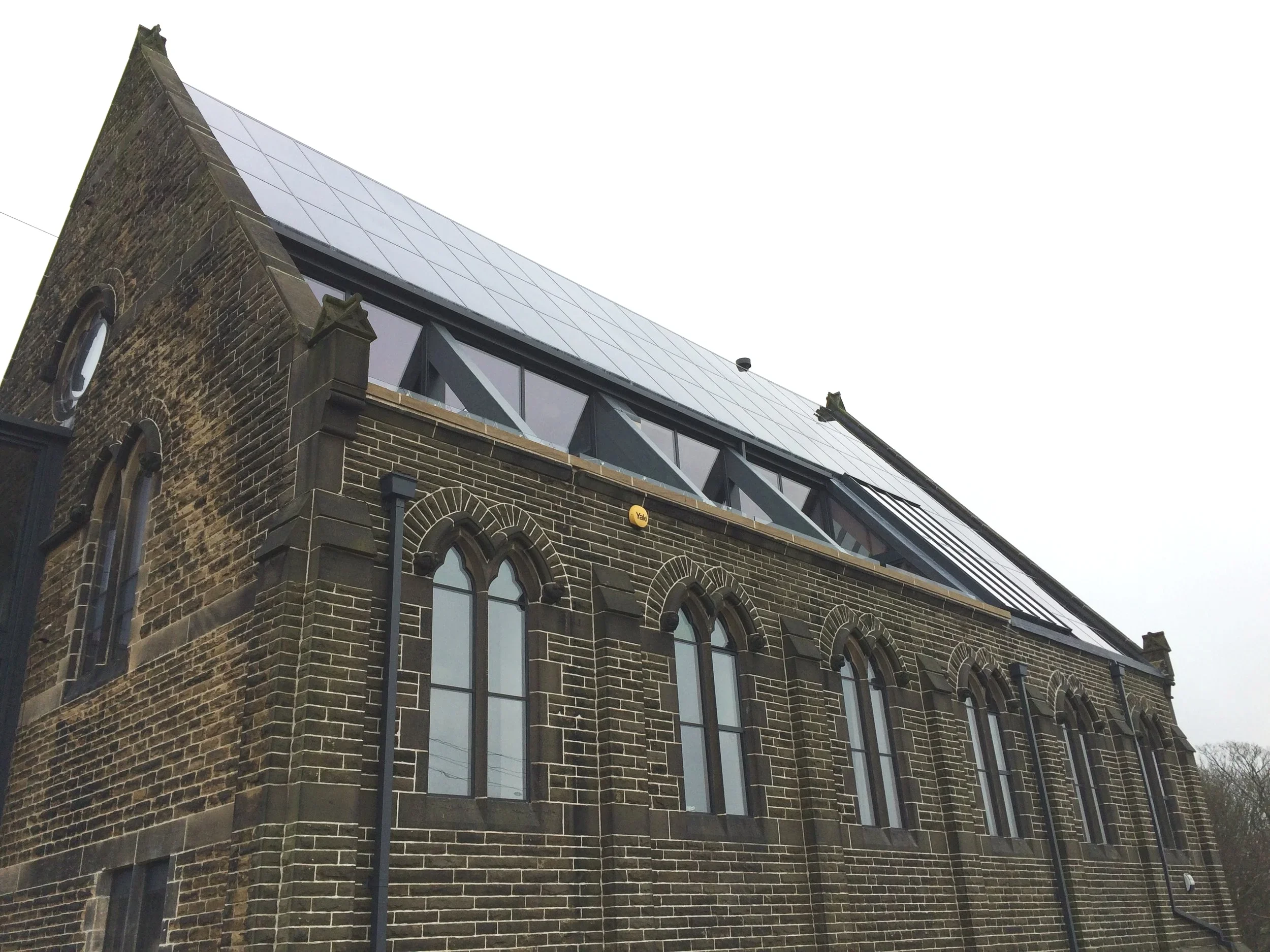 A brick building with large arched windows and a modern glass and metal extension at the top, under an overcast sky.
