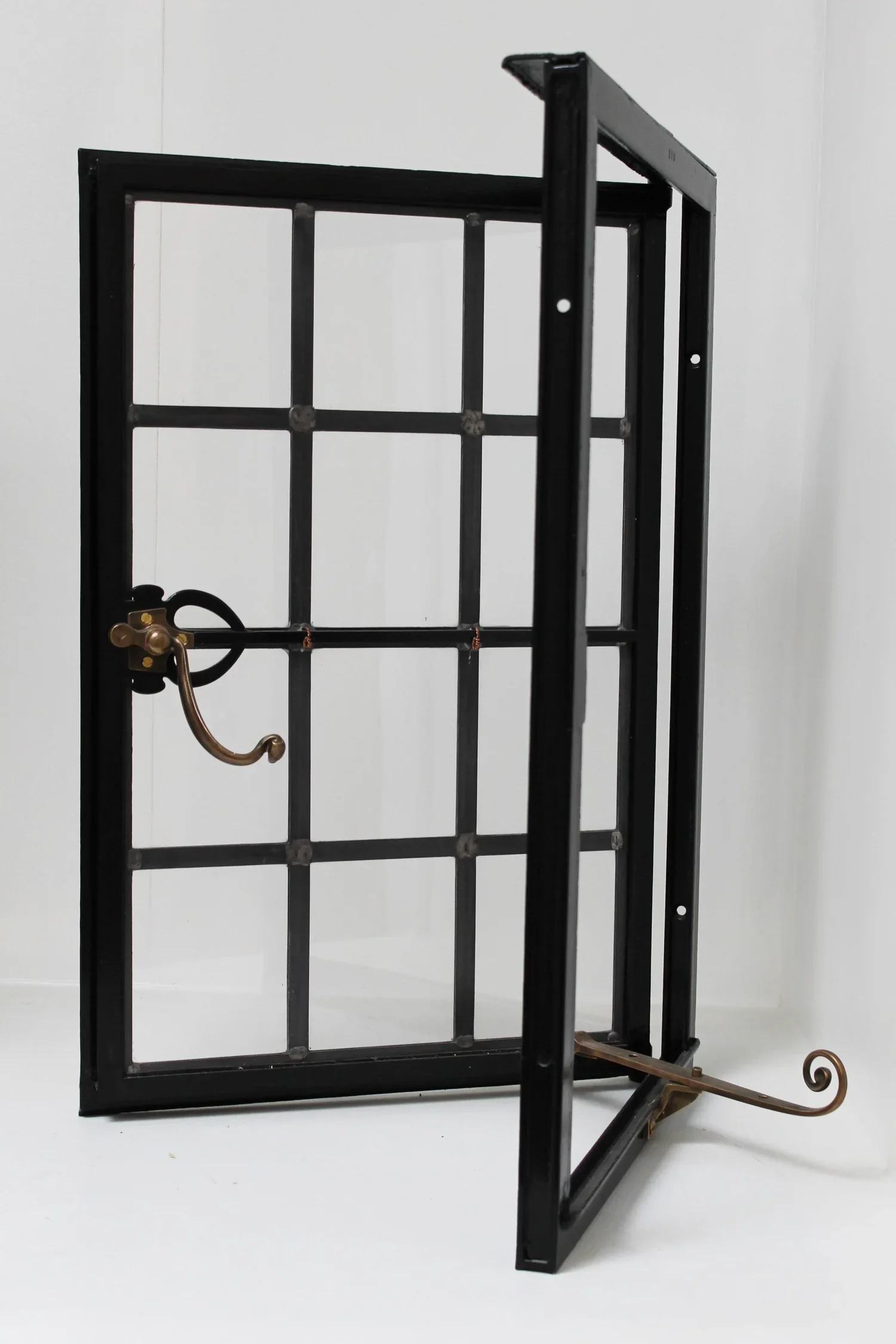 A black metal window frame with a small brass hook attached to one side, leaning against a plain white wall.