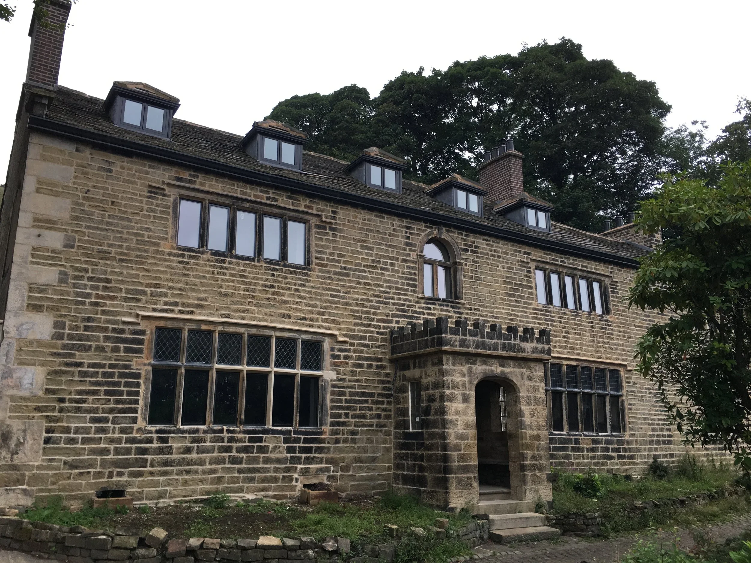 A historic stone building with multiple windows and an arched entrance, surrounded by trees.
