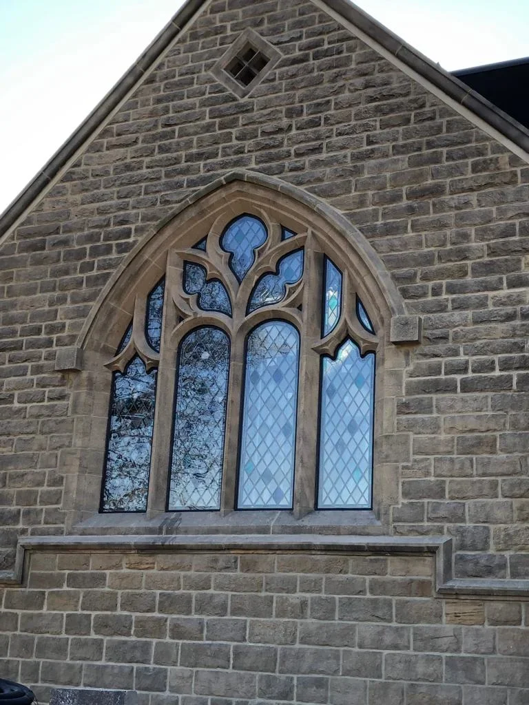Close-up of a Gothic-style stained glass window on a brick church wall.