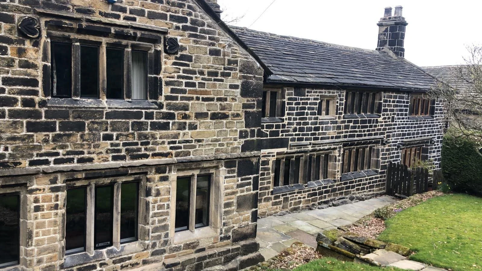 Photo of a historic stone house with multiple small windows and a garden in the foreground.