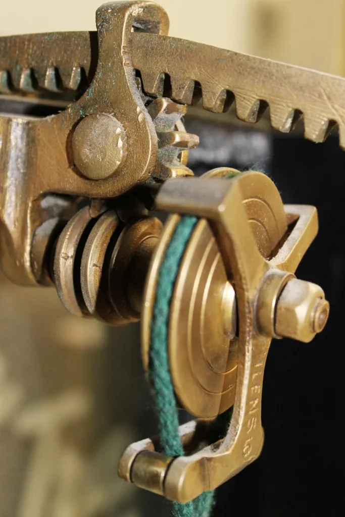 Close-up of a vintage mechanical musical instrument part with gears, wheels, and a threaded component, made of brass or similar metal.