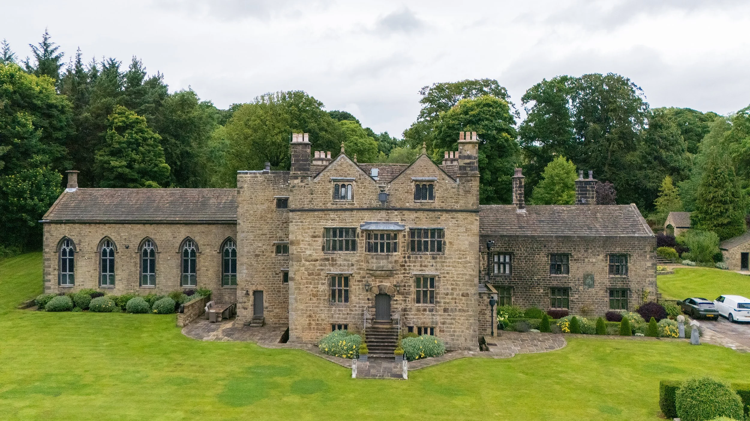 Stone mansion with multiple gothic-style windows, surrounded by a manicured lawn and trees in the background.