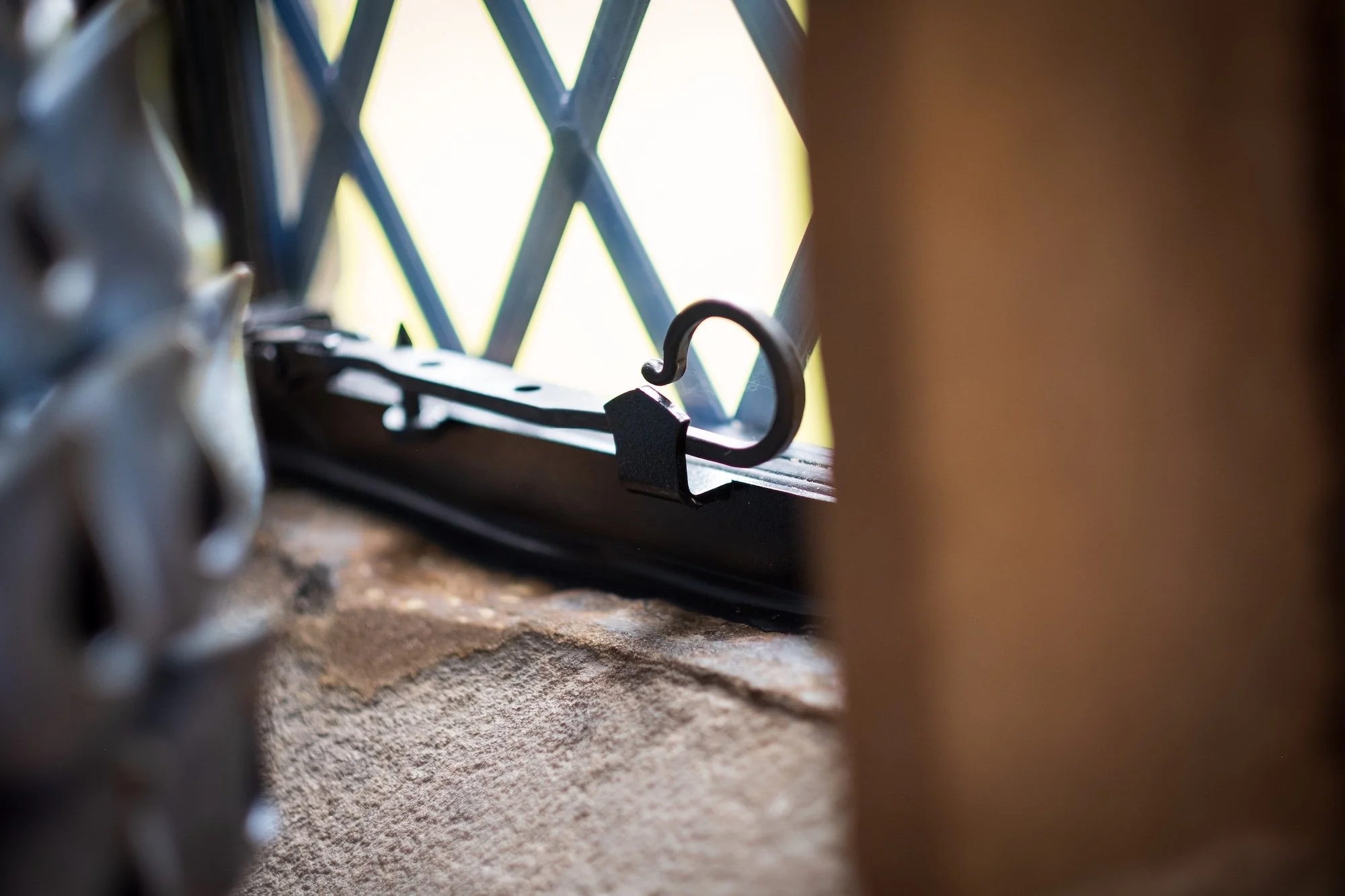 Close-up of a black latch or hook on a metal surface in front of a window with a yellow lattice pattern.