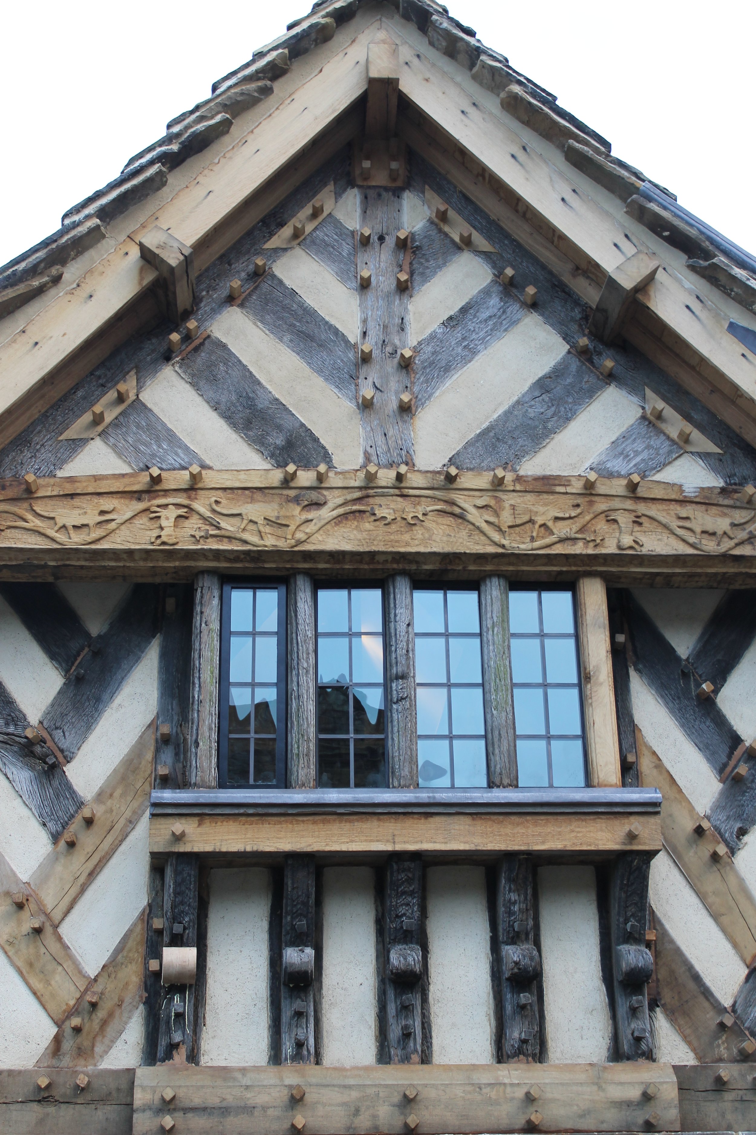 Close-up of a building's gable end showing decorative half-timbered woodwork and a window with grid-patterned panes.
