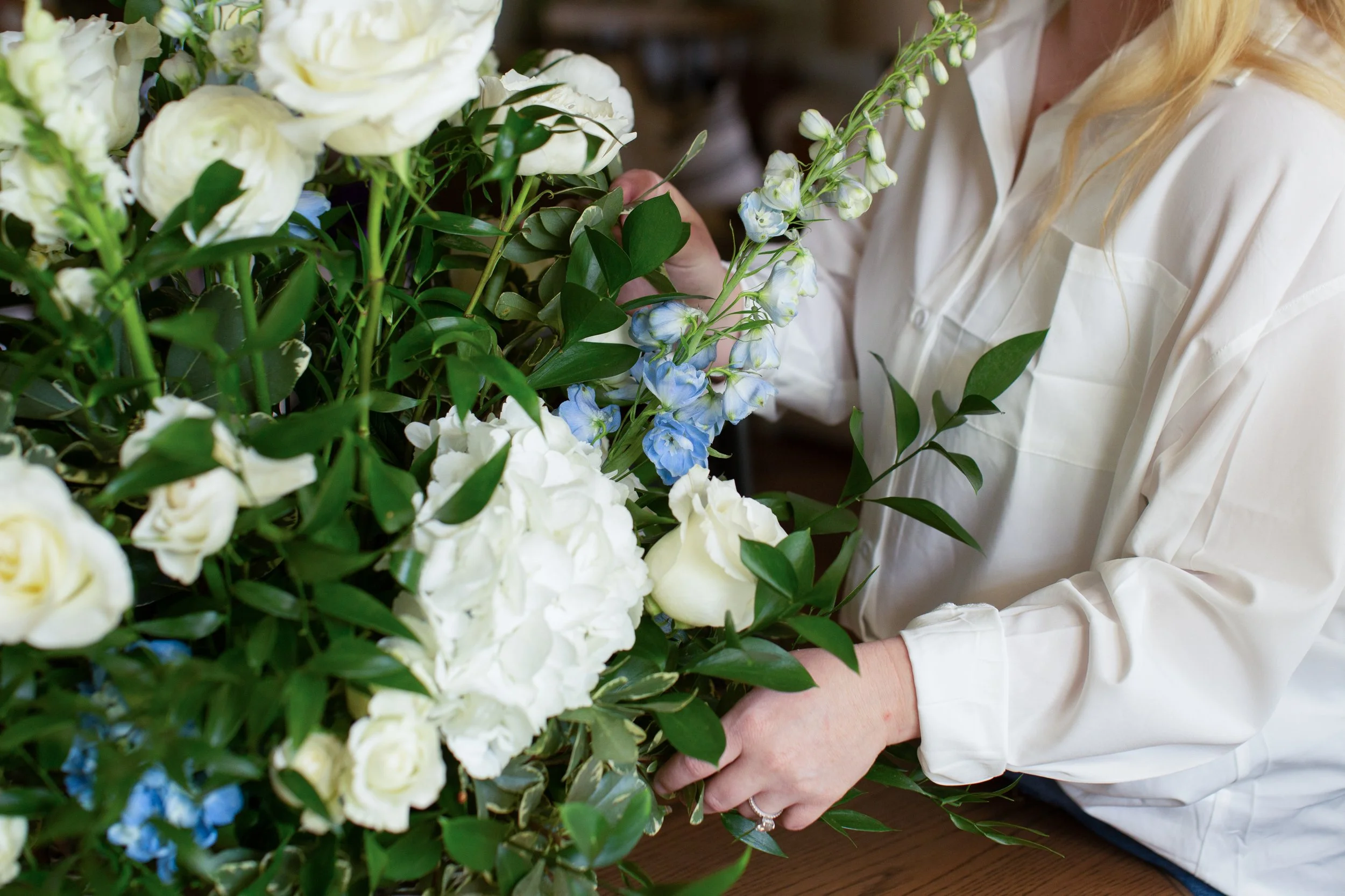 Wedding floral arrangement of white hydrangeas, roses, and delphinium being created by a florist in Central Louisiana.