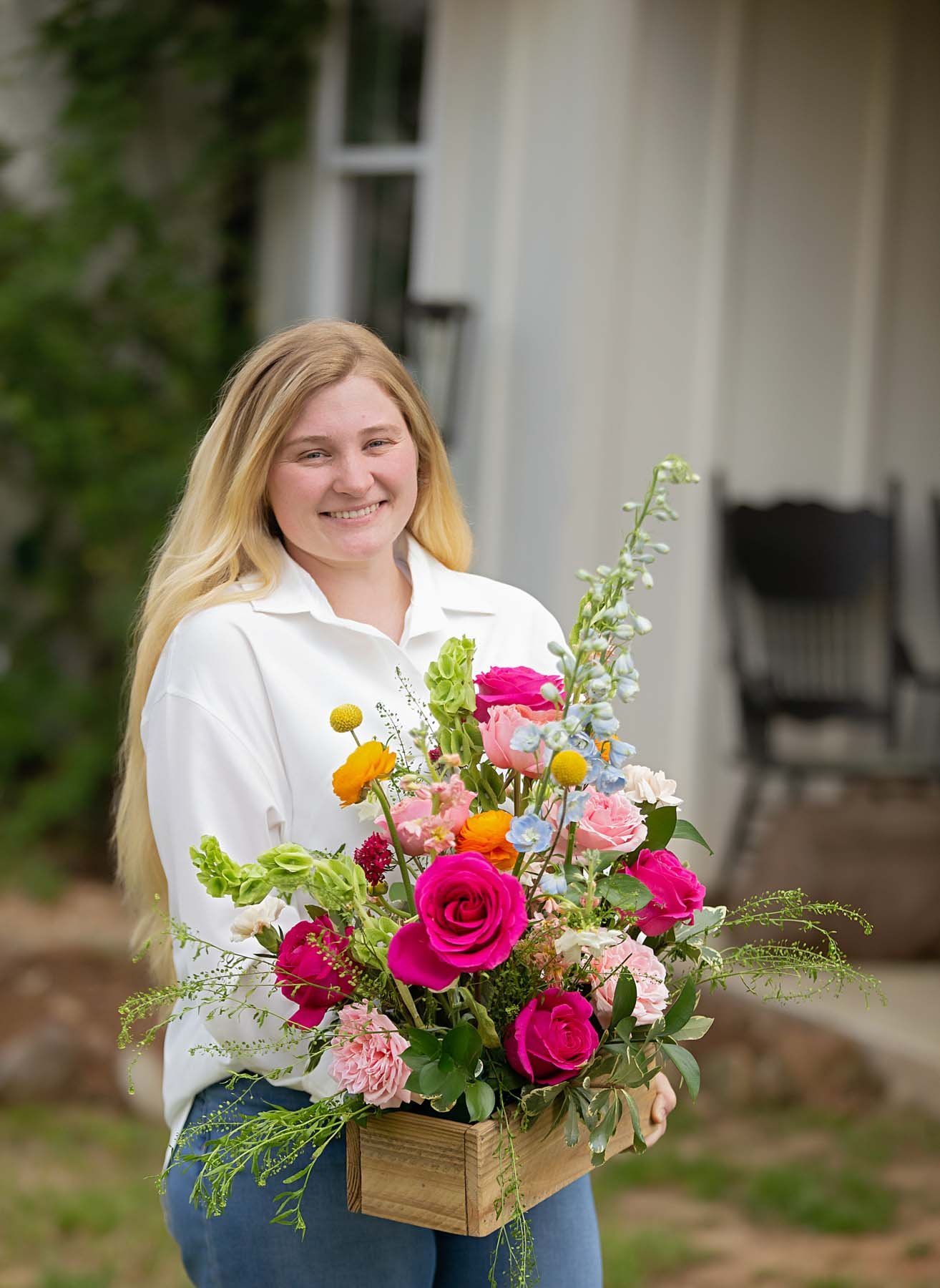 Central louisiana florist holding a box of pink flowers in front of a house.