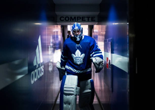 Hockey goalie in Toronto Maple Leafs uniform walking through a tunnel onto the ice rink.