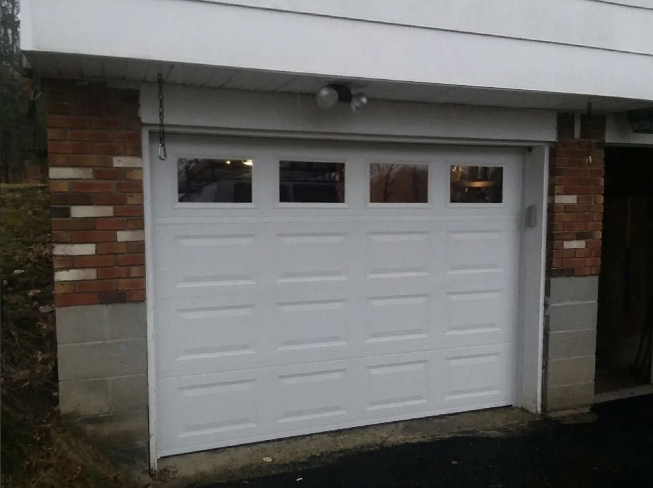 White garage door with four small windows at the top, set in a brick building with a concrete base.