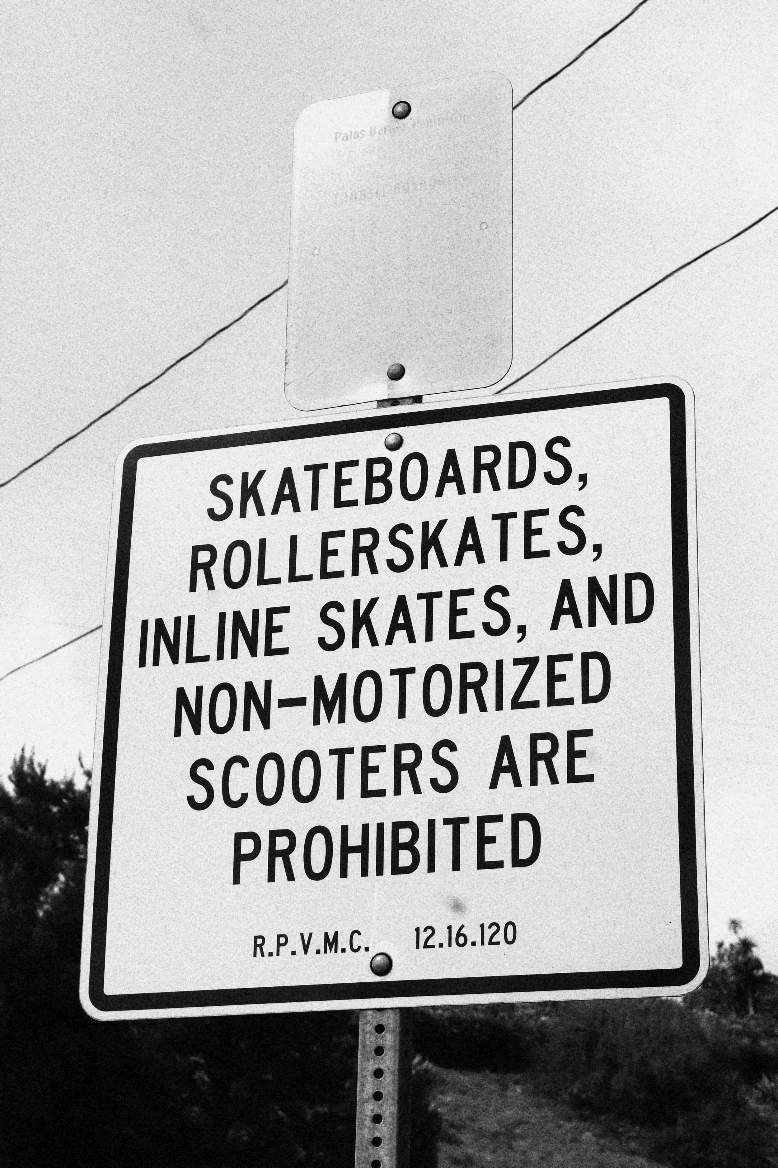 A black-and-white sign indicating that skateboards, roller skates, inline skates, and non-motorized scooters are prohibited.